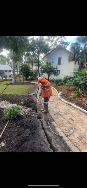 A Person in Work Gear Working on Landscaping Near a Brick Path and Trees — Tyzac Group in Beerwah, QLD