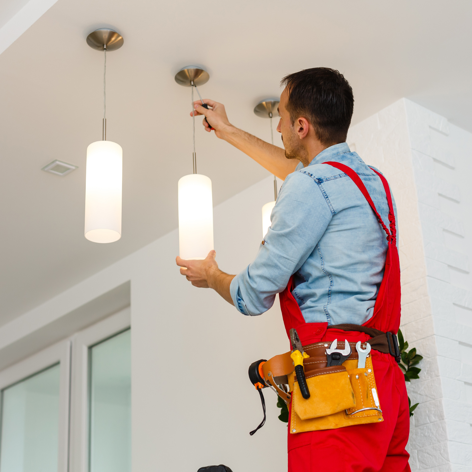 Electrician installing a pendant light fixture on a white ceiling.