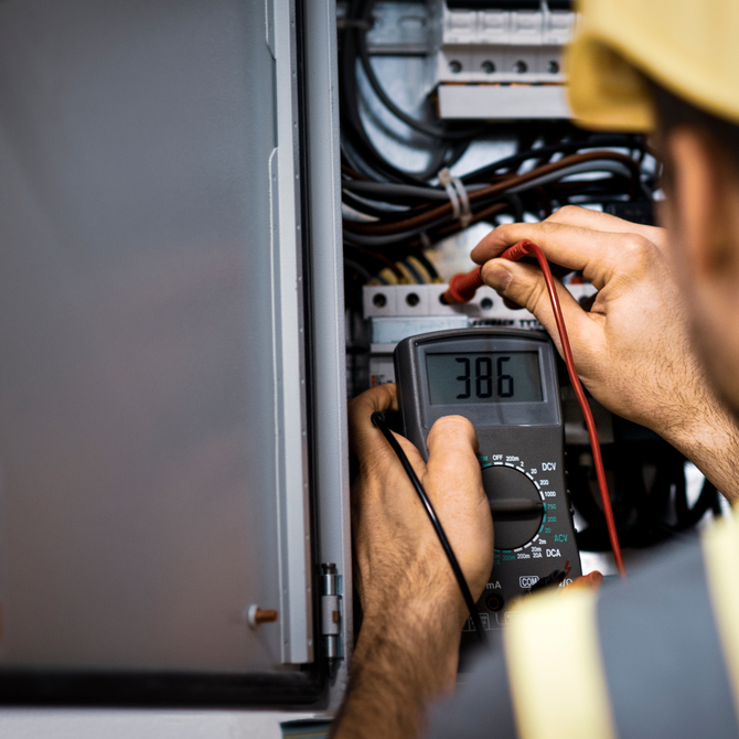 Man inspecting an open electrical panel with a flashlight in a garage.