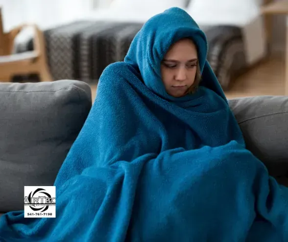 A woman wrapped in a blue blanket is sitting on a couch.
