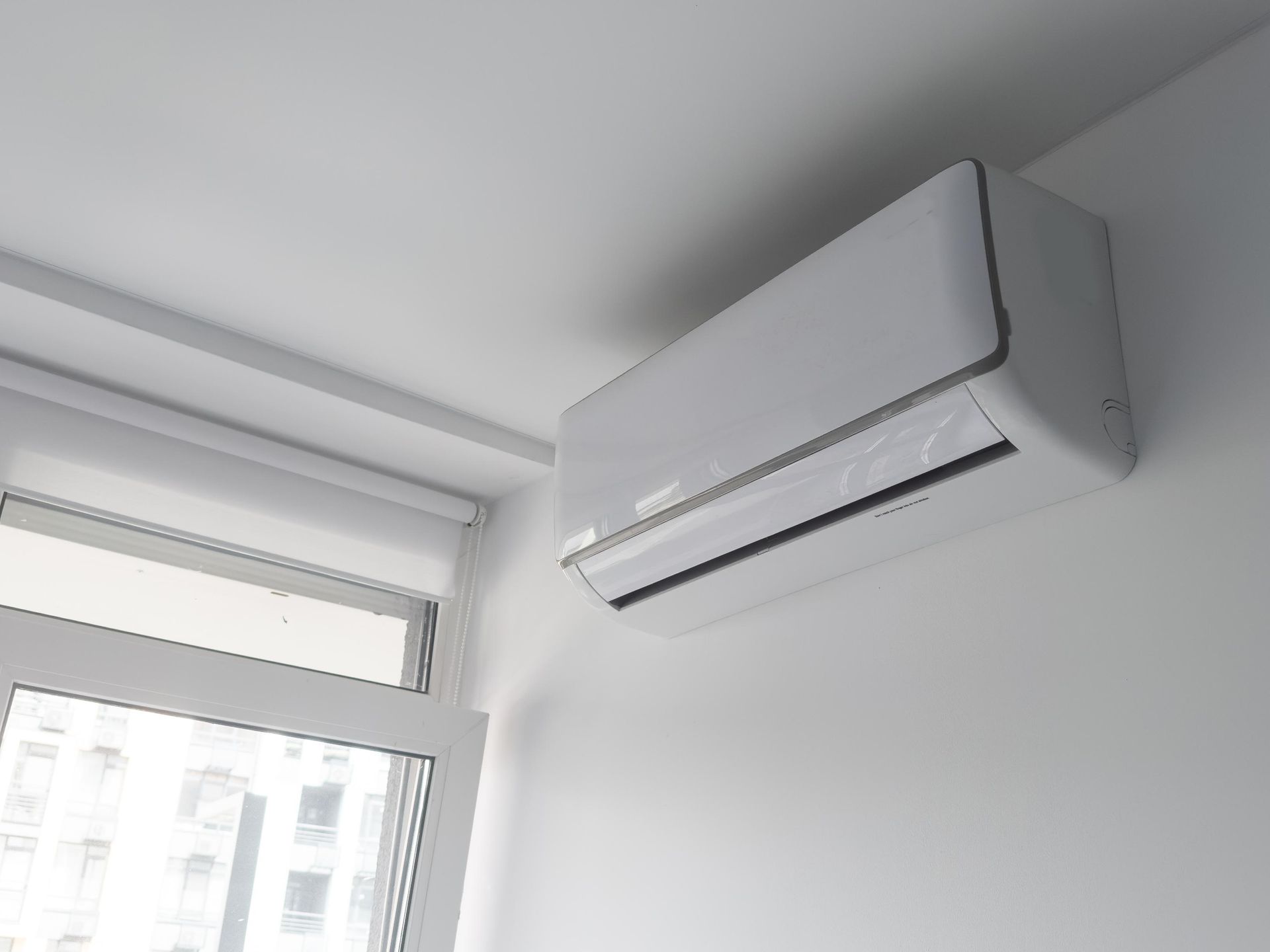 A white air conditioner is mounted to the wall next to a window.