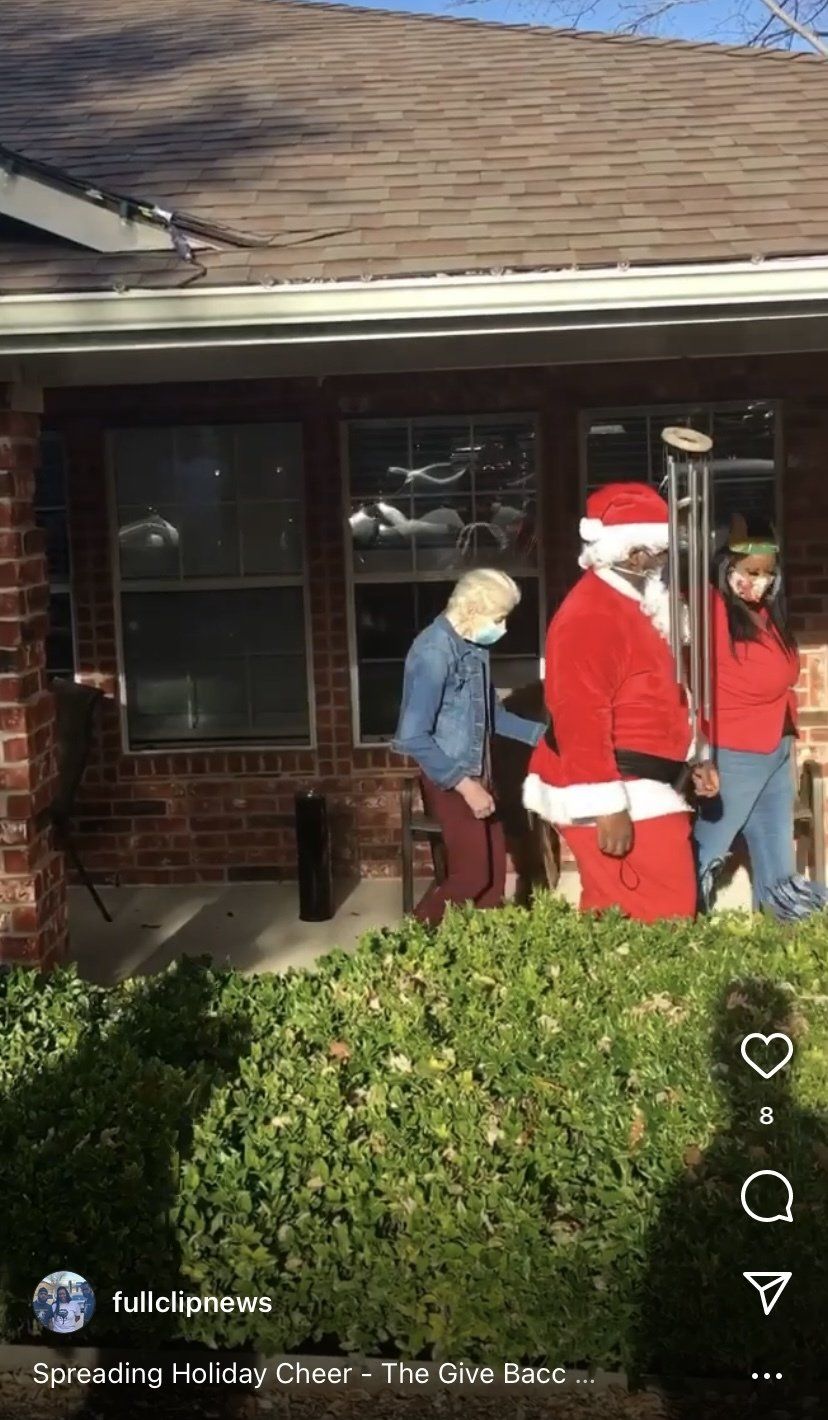 A man dressed as santa claus is standing in front of a brick house
