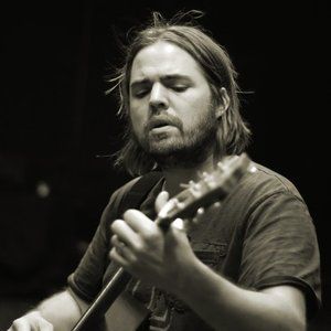 Man with long hair playing acoustic guitar. Dark setting, sepia tone.