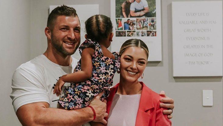 Man holding child, woman smiling, all posed in front of wall with photos.