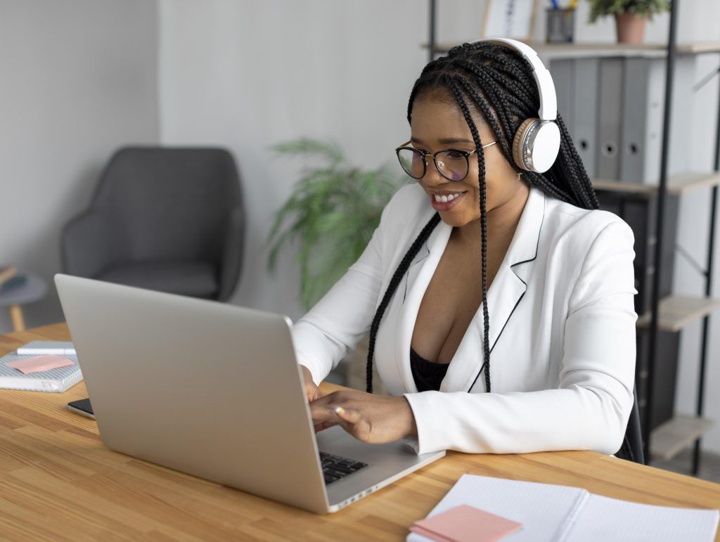 A woman wearing headphones is sitting at a desk using a laptop computer.