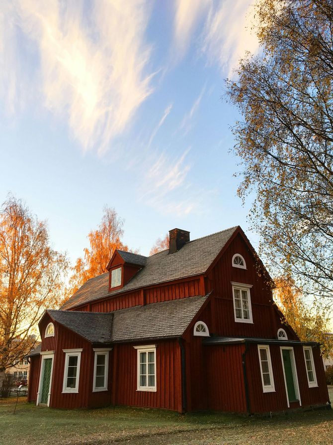 A red house with a gray roof is surrounded by trees and a blue sky.