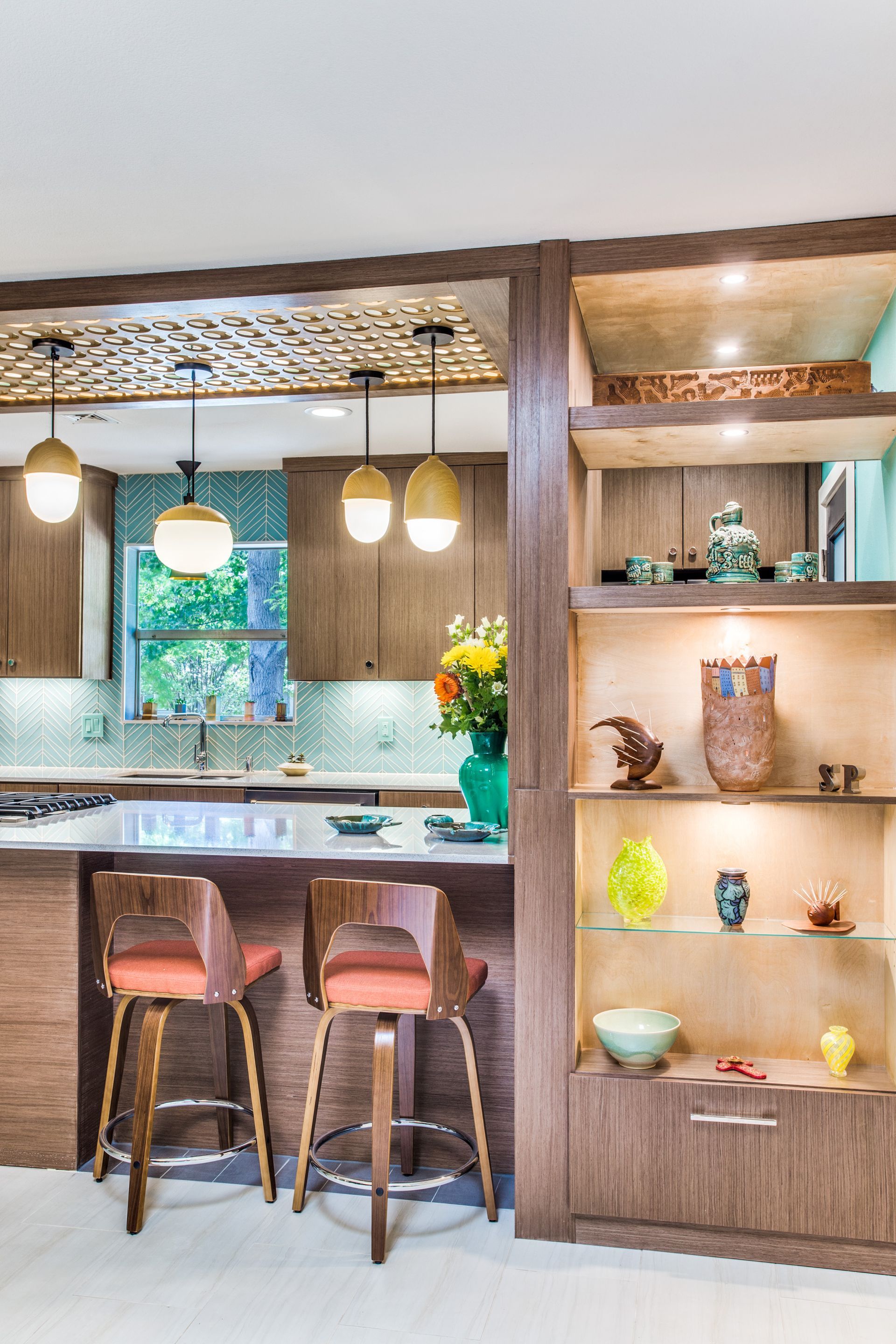 A kitchen with a bar , stools , shelves and a window.