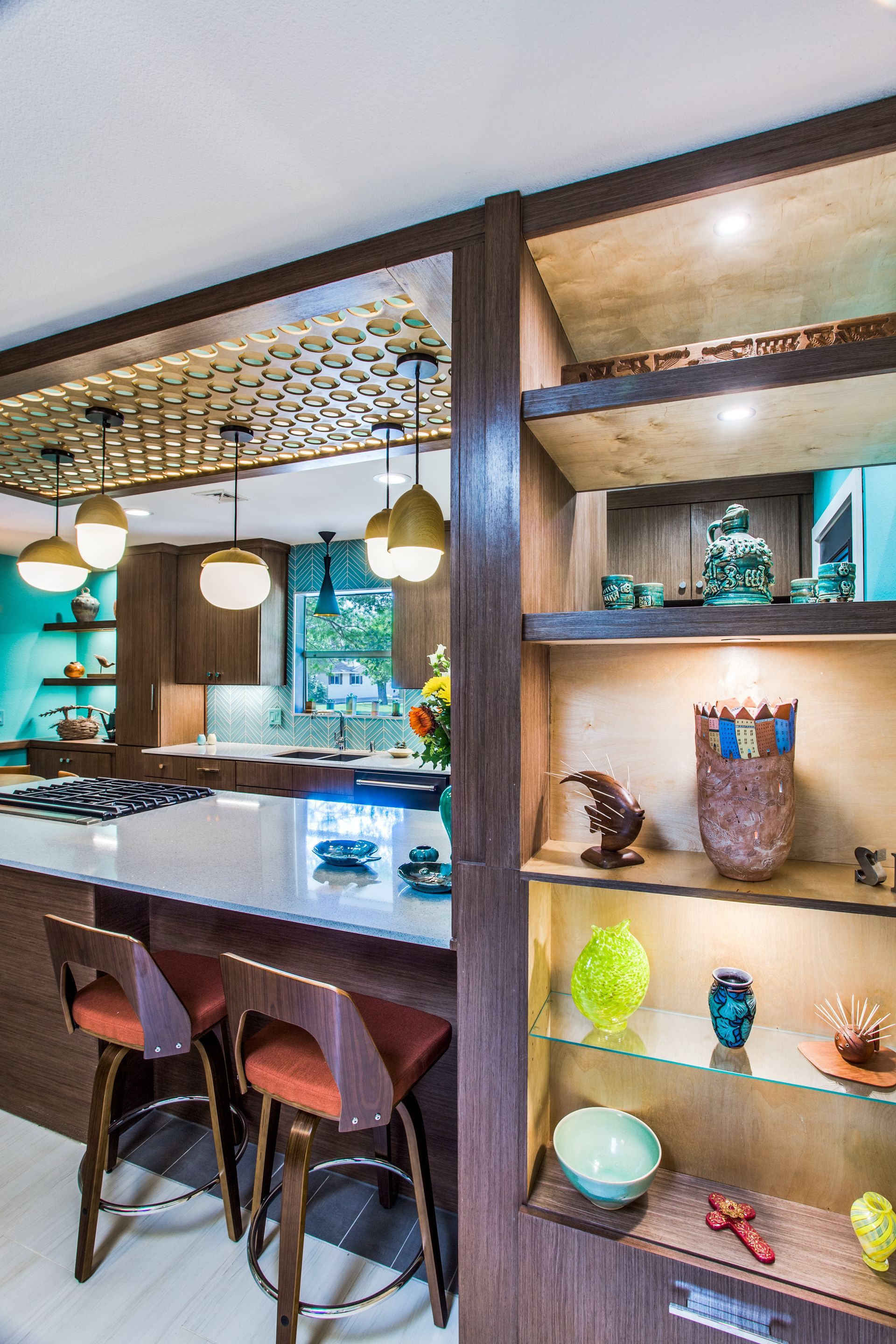 A kitchen with a bar , stools , shelves and a stove.