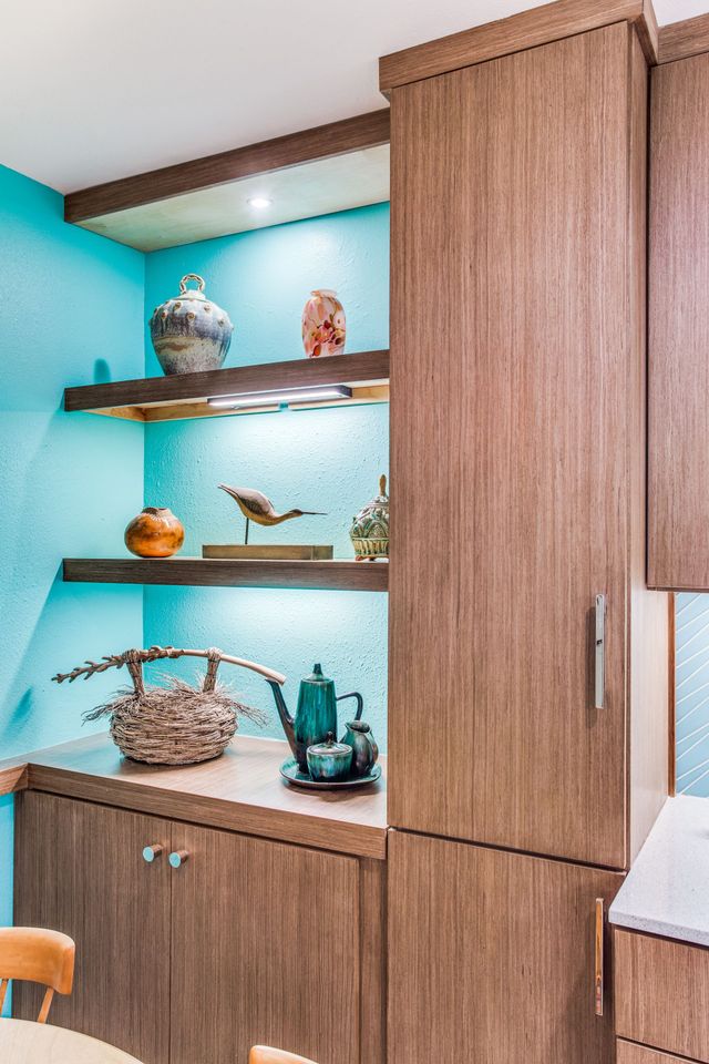 A kitchen with wooden cabinets and shelves and a blue wall.