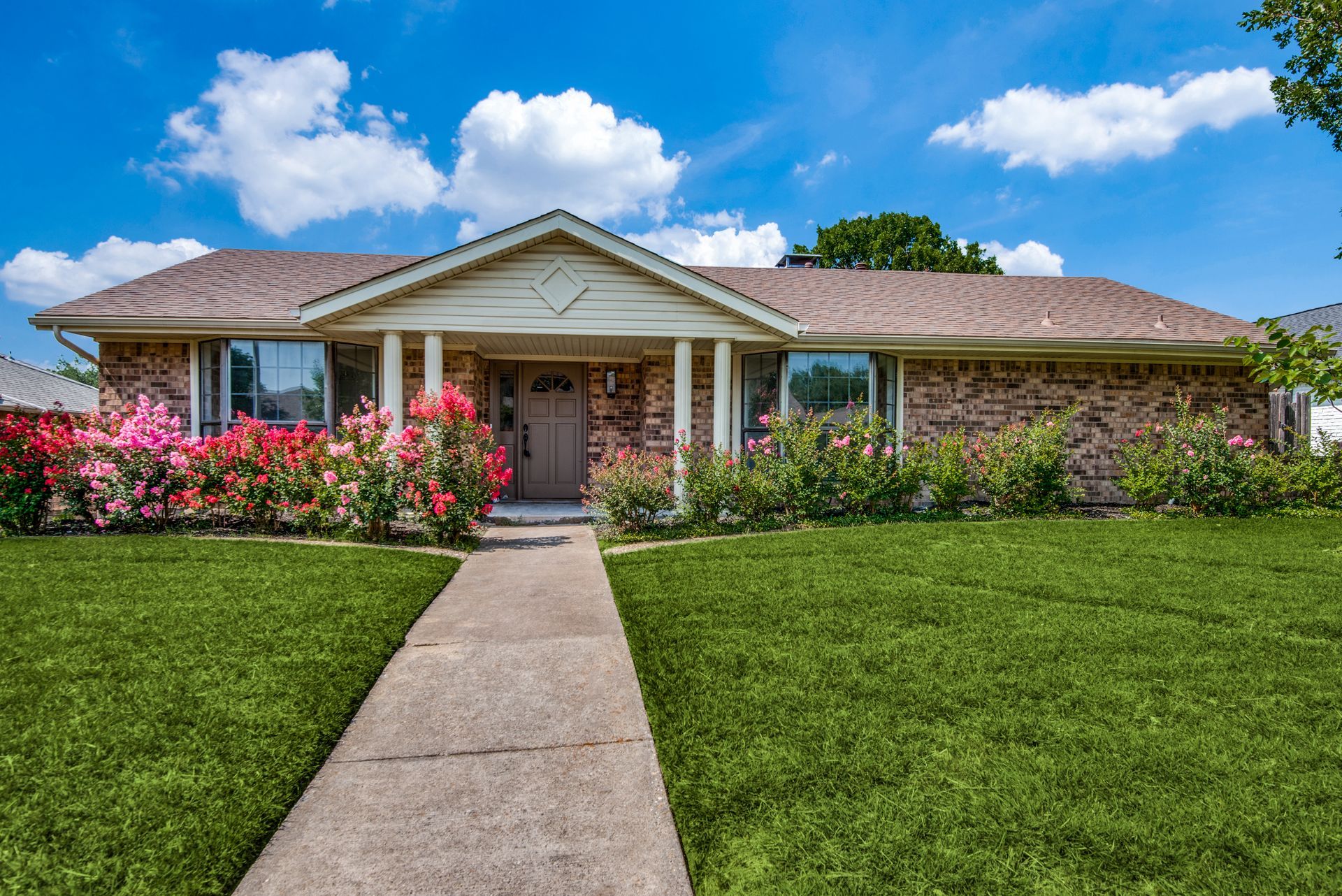 A brick house with a lush green lawn and a concrete walkway leading to it.