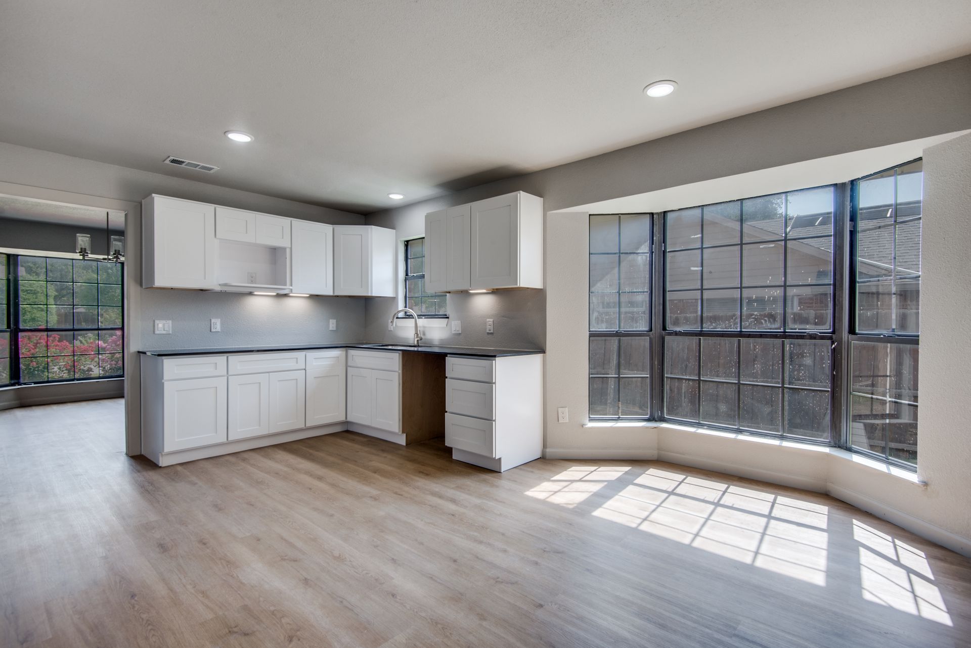 An empty kitchen with white cabinets and a large window.