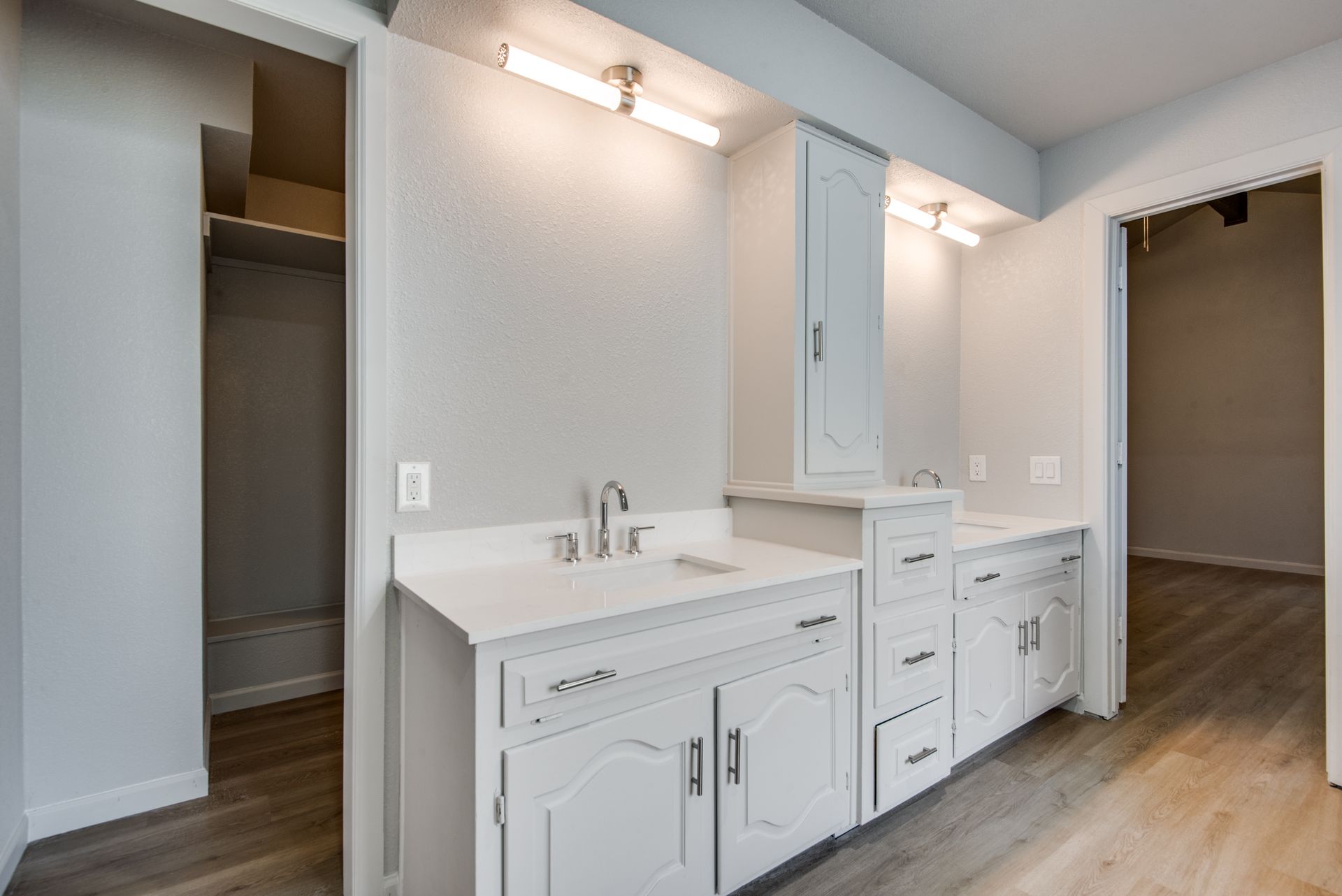 A bathroom with white cabinets , a sink , and a walk in closet.