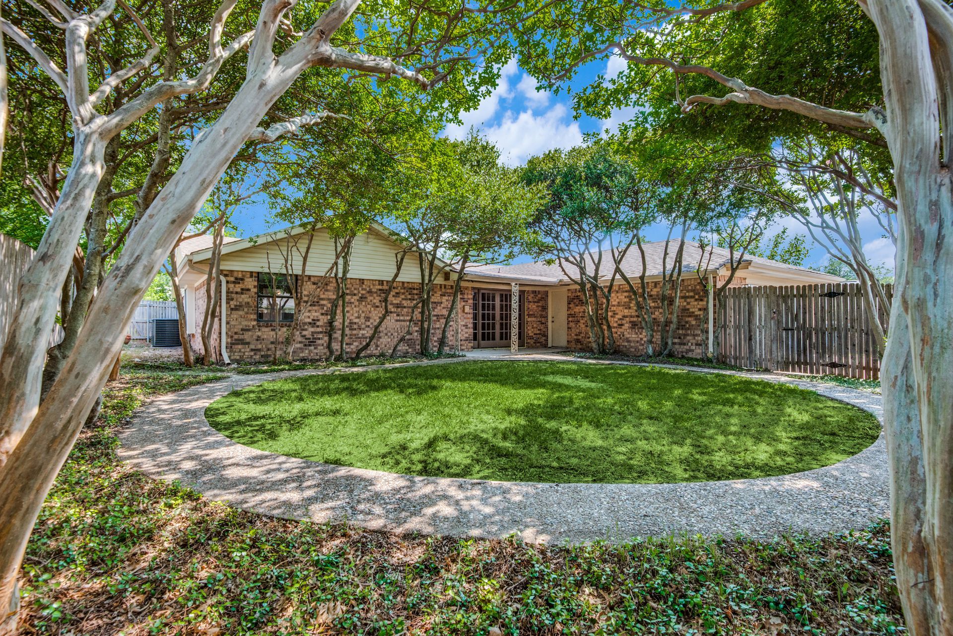 A house remodel with a large circular lawn in front of it surrounded by trees.