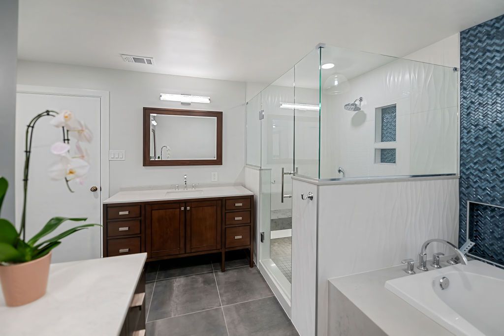 A bathroom with a tub , sink , mirror and shower.