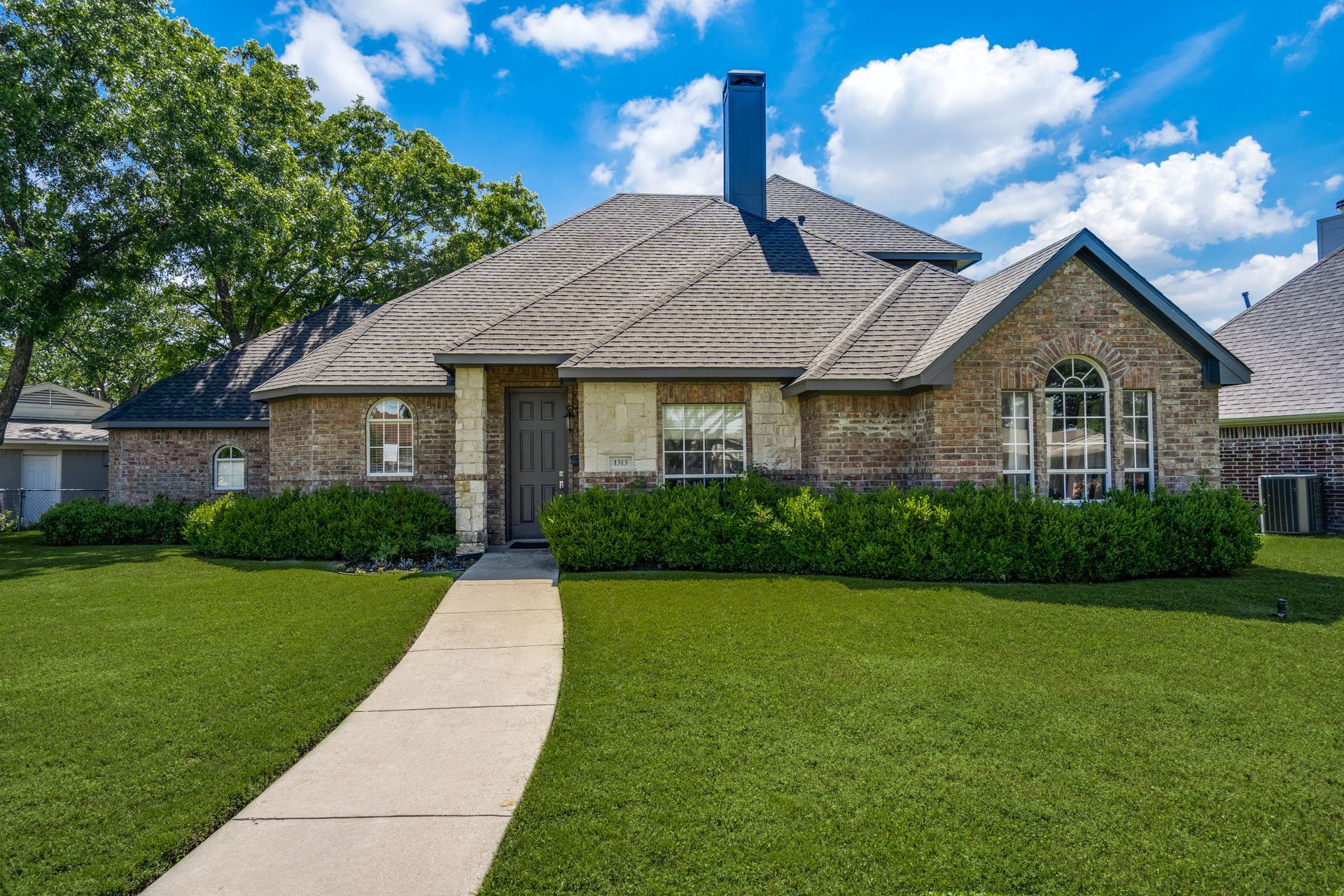 A brick house remodel with a lush green lawn and a walkway leading to it.