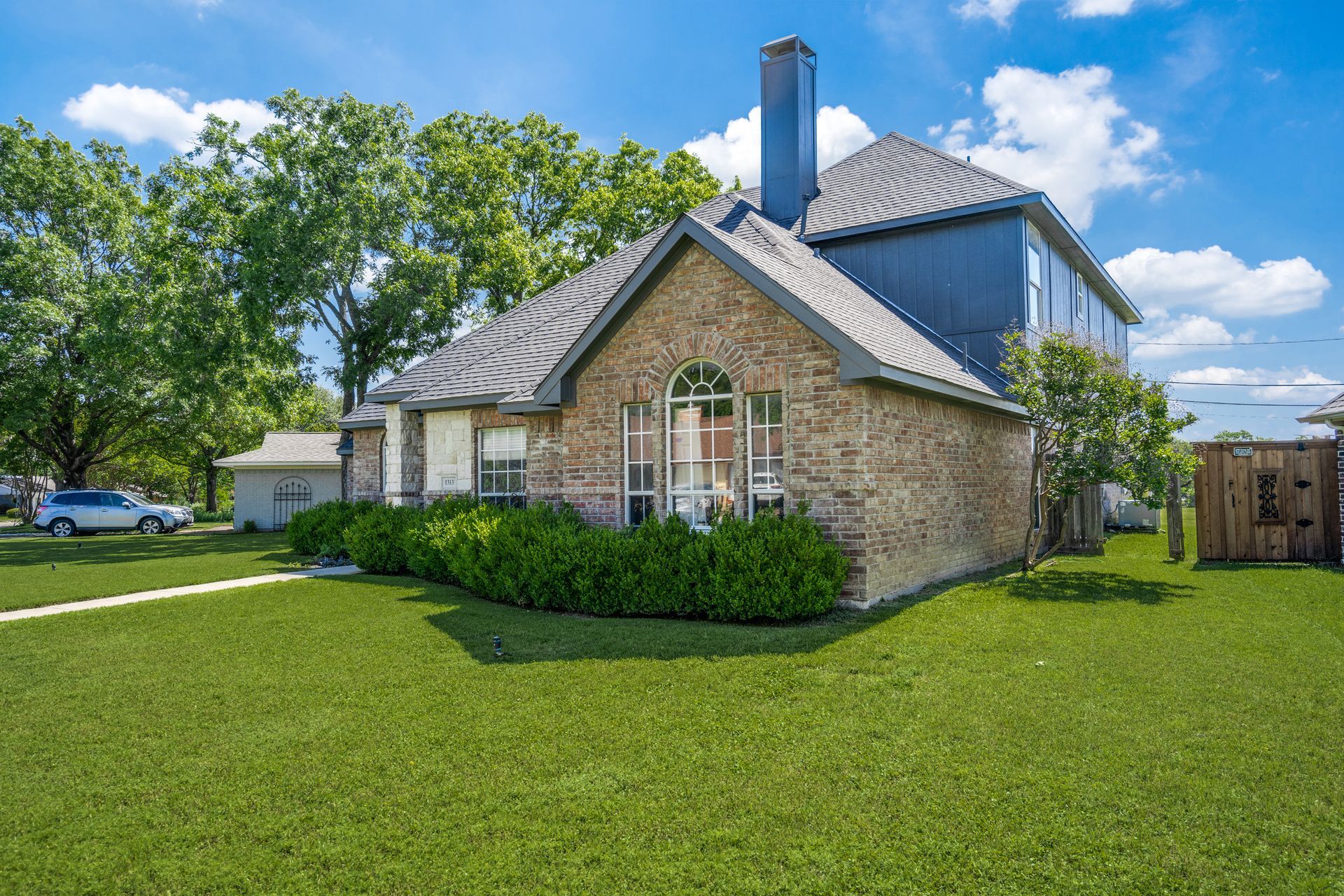 A small brick house remodel  with a large lawn in front of it.