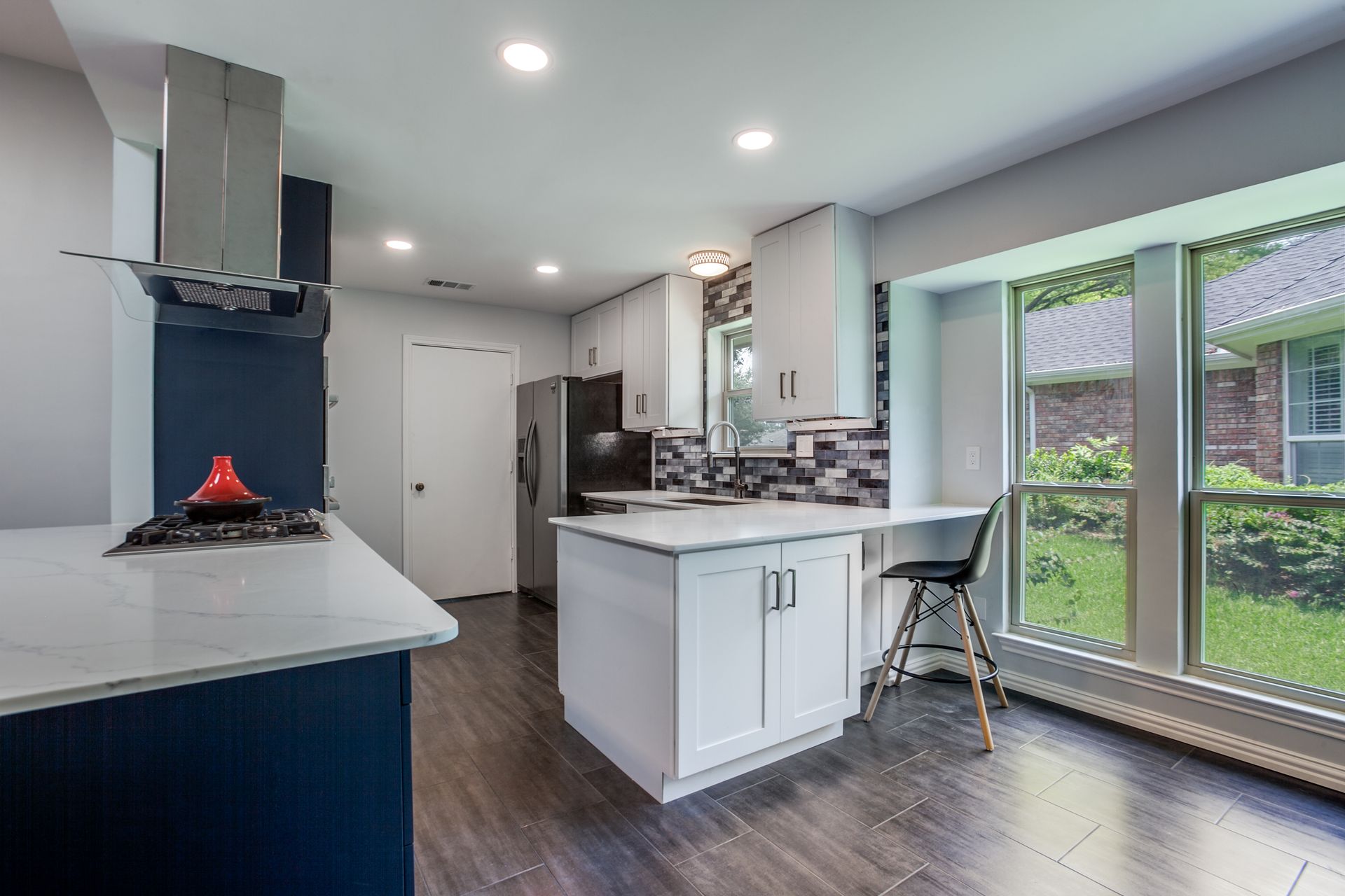 A kitchen with white cabinets , a large island , a refrigerator , and a large window.
