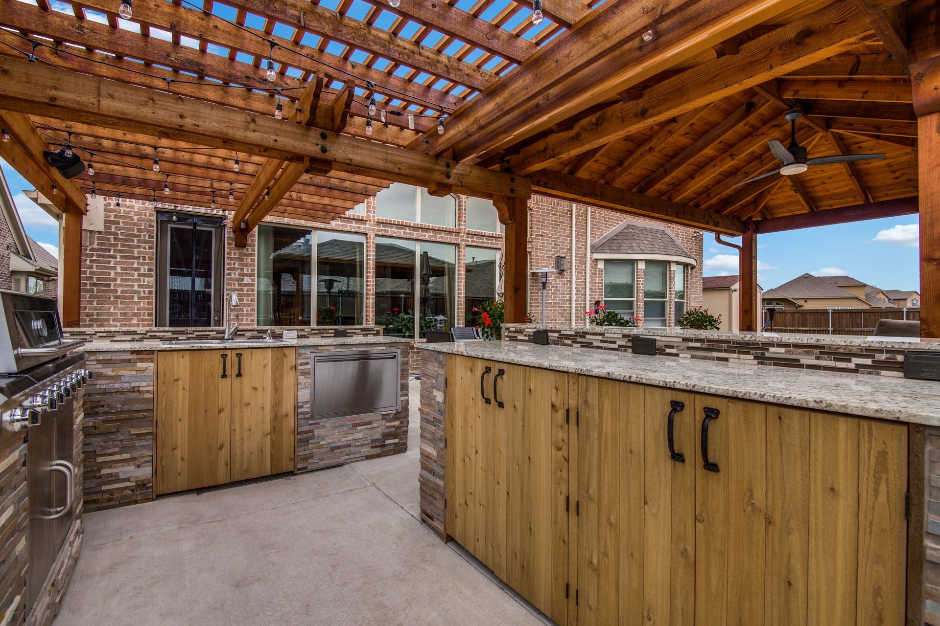 A large outdoor kitchen remodel with a wooden pergola over it.