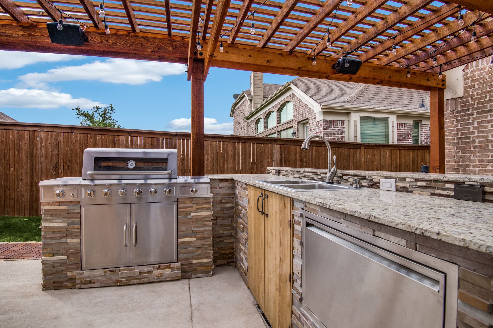 An outdoor kitchen with a grill , sink , and pergola.