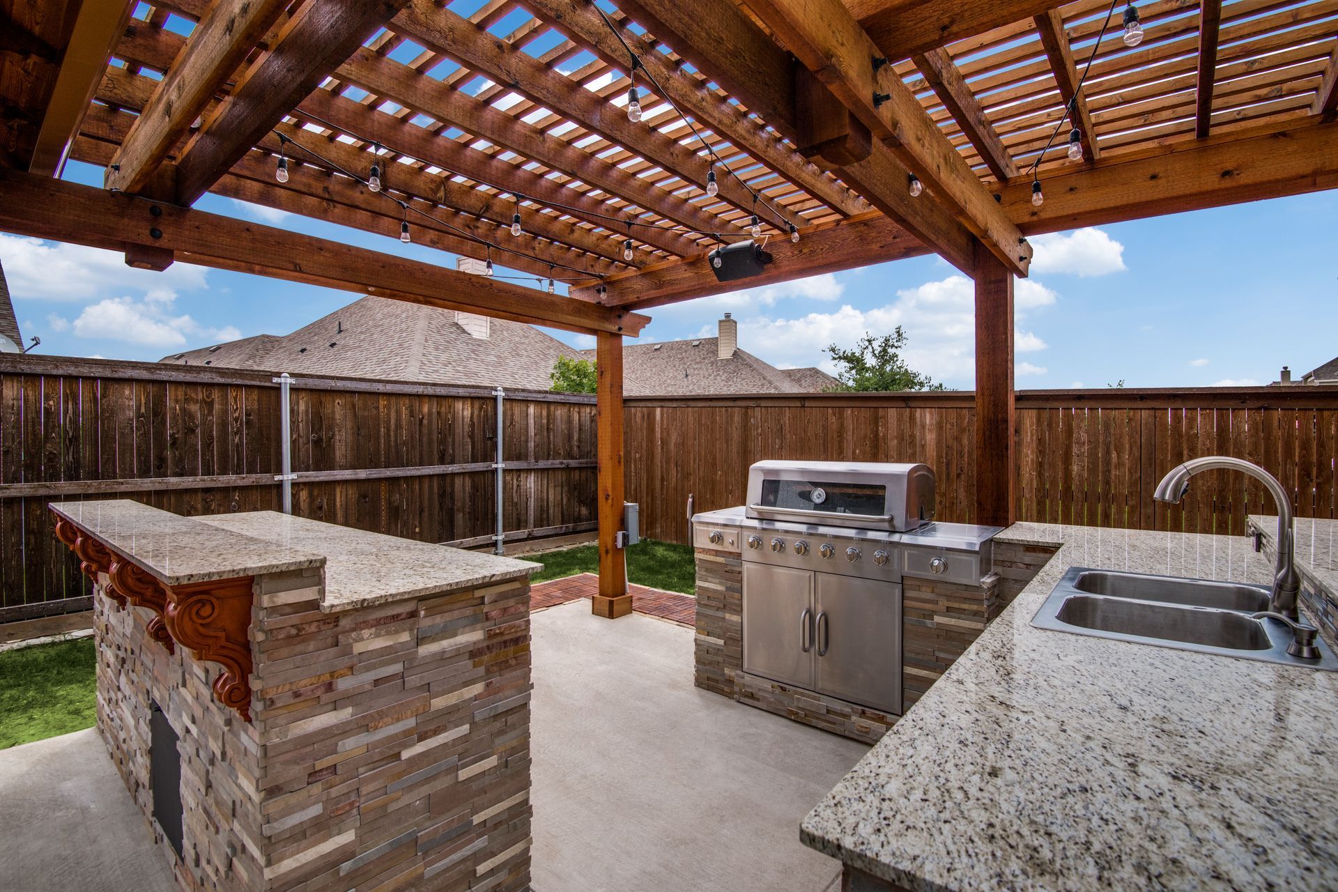 A kitchen remodel with granite counter tops and a grill under a pergola.