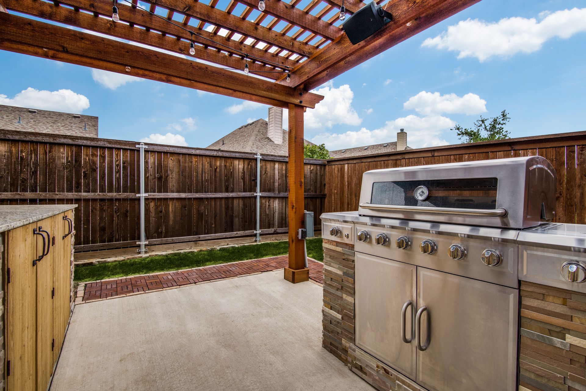 A stainless steel grill is sitting under a wooden pergola remodel in a backyard.