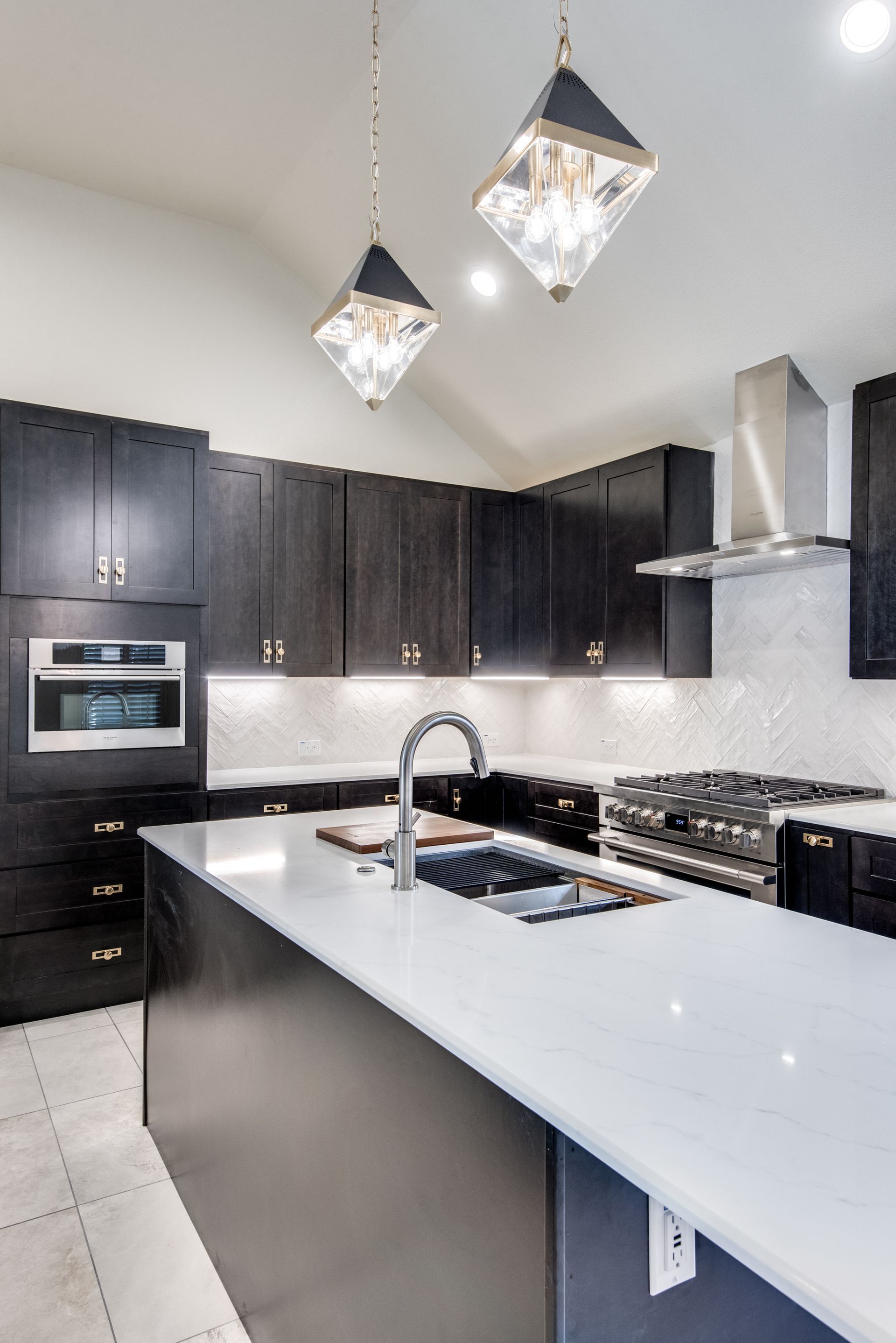 A kitchen with black cabinets , white counter tops , stainless steel appliances and a large island.