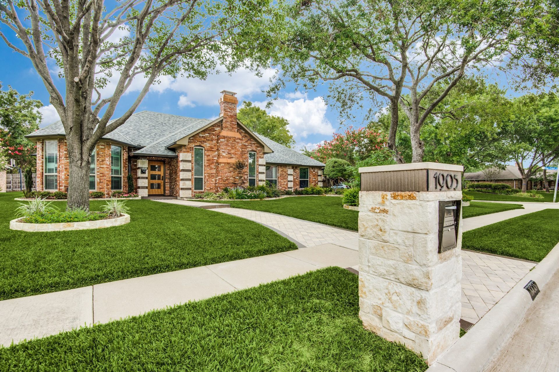 A brick house remodel with a lush green lawn and a stone mailbox in front of it.