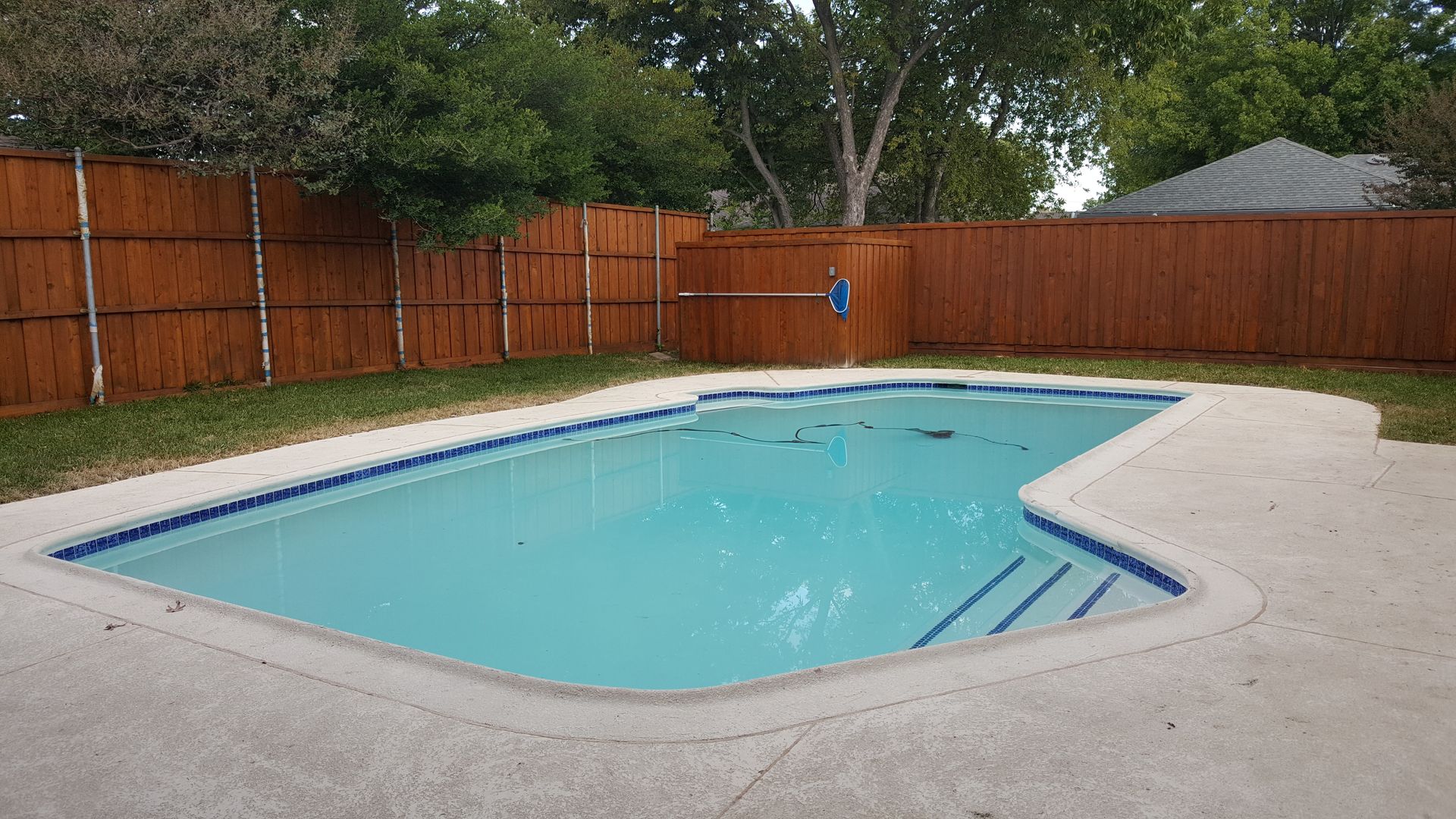 A large swimming pool surrounded by a wooden fence in a backyard.