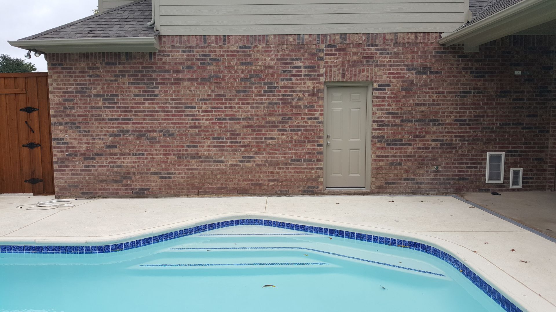 A brick house remodel with a swimming pool in front of it.