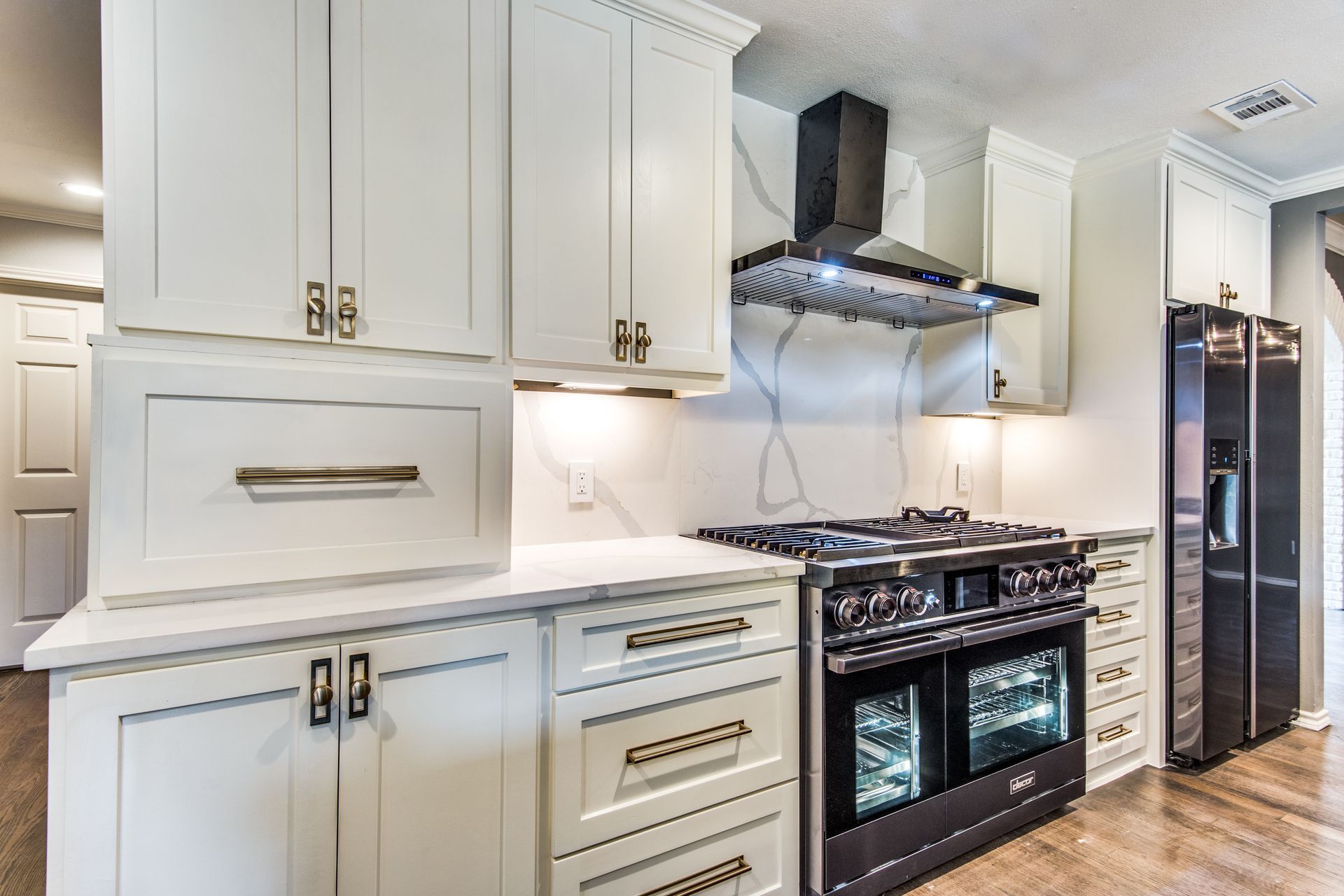 A kitchen with white cabinets , a stove , a refrigerator , and a hood.
