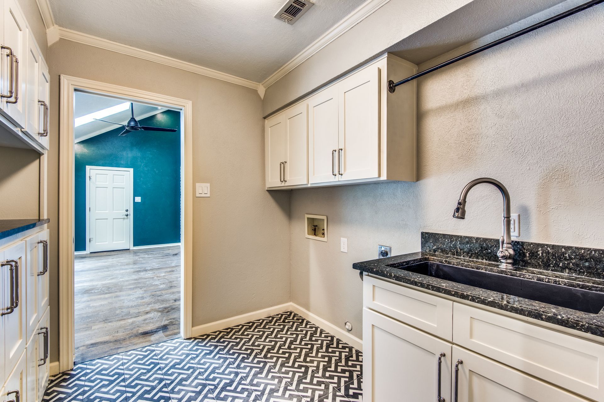 A laundry room with a sink and cabinets in a house.