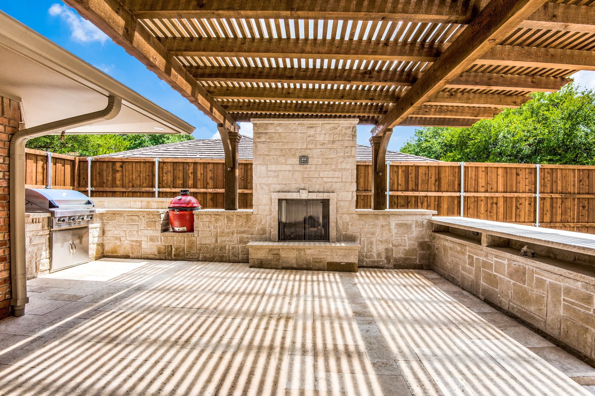 A patio with a fireplace and a grill under a wooden pergola.