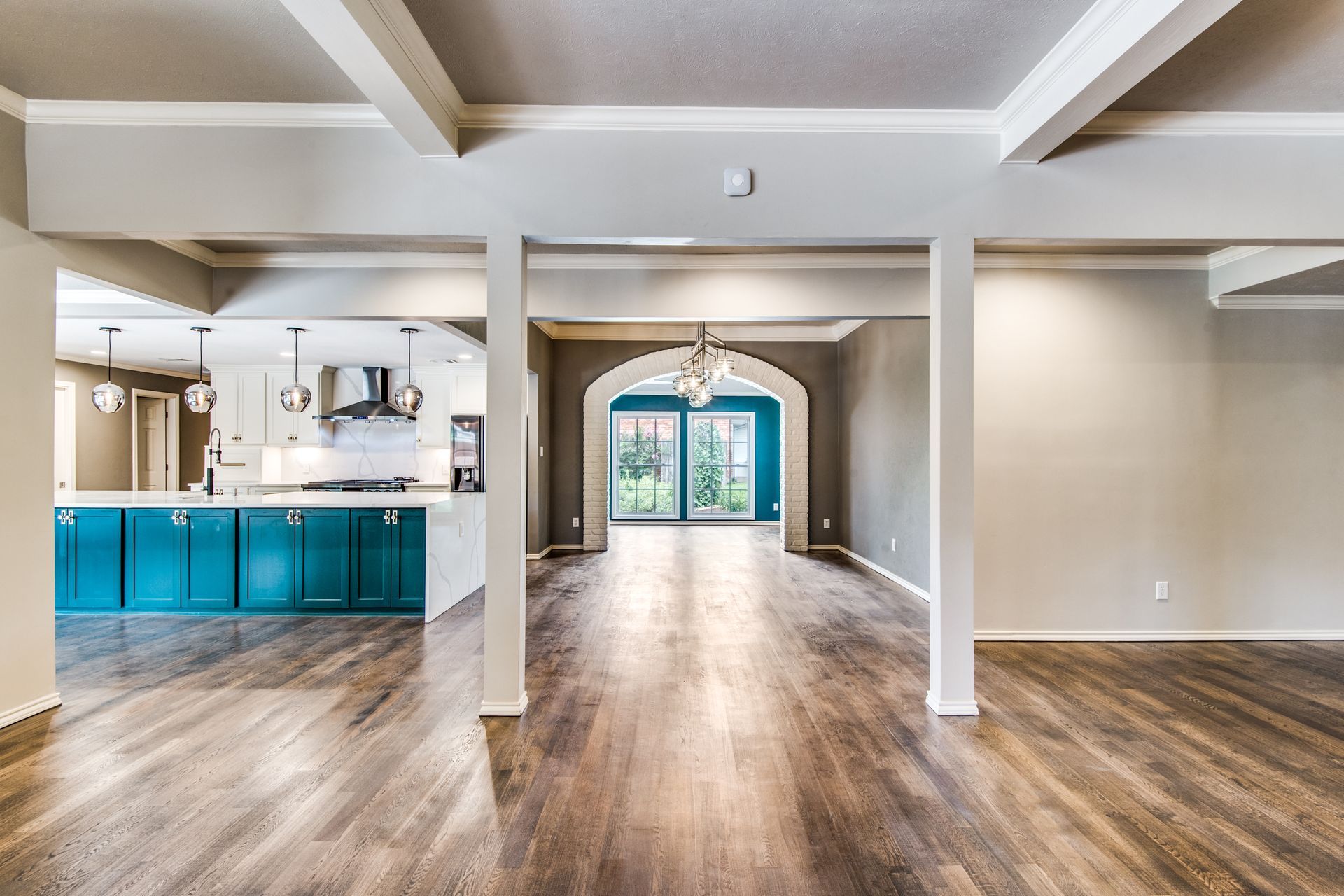 A large empty room with hardwood floors and a kitchen in the background.