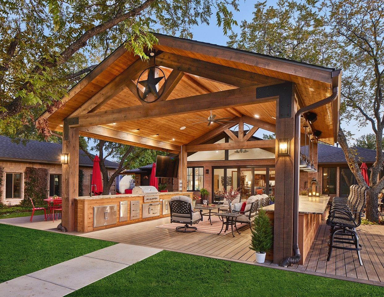 A large wooden pavilion with a texas star on the roof is in the backyard of a house.