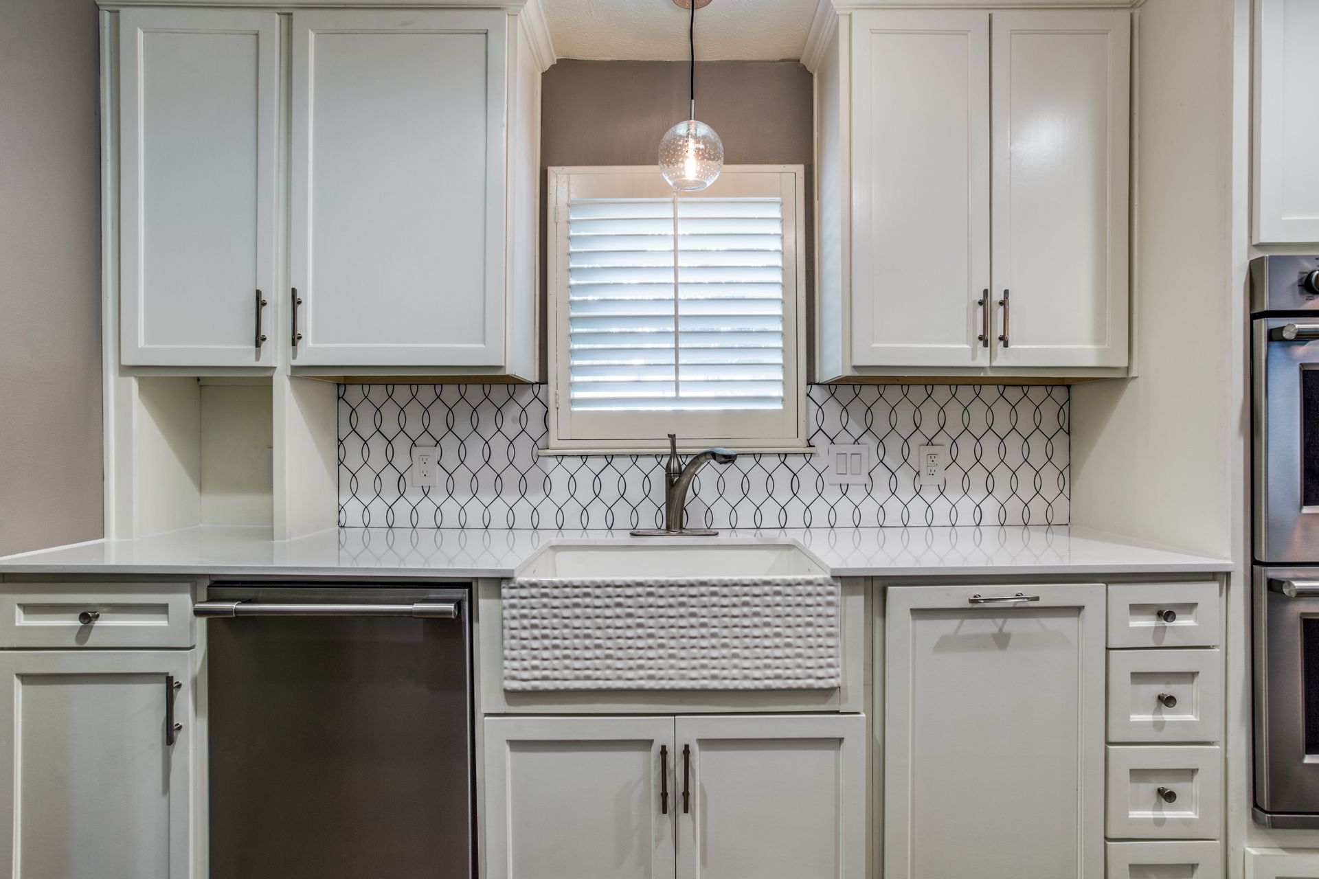 A kitchen with white cabinets , stainless steel appliances , a sink , and a window.