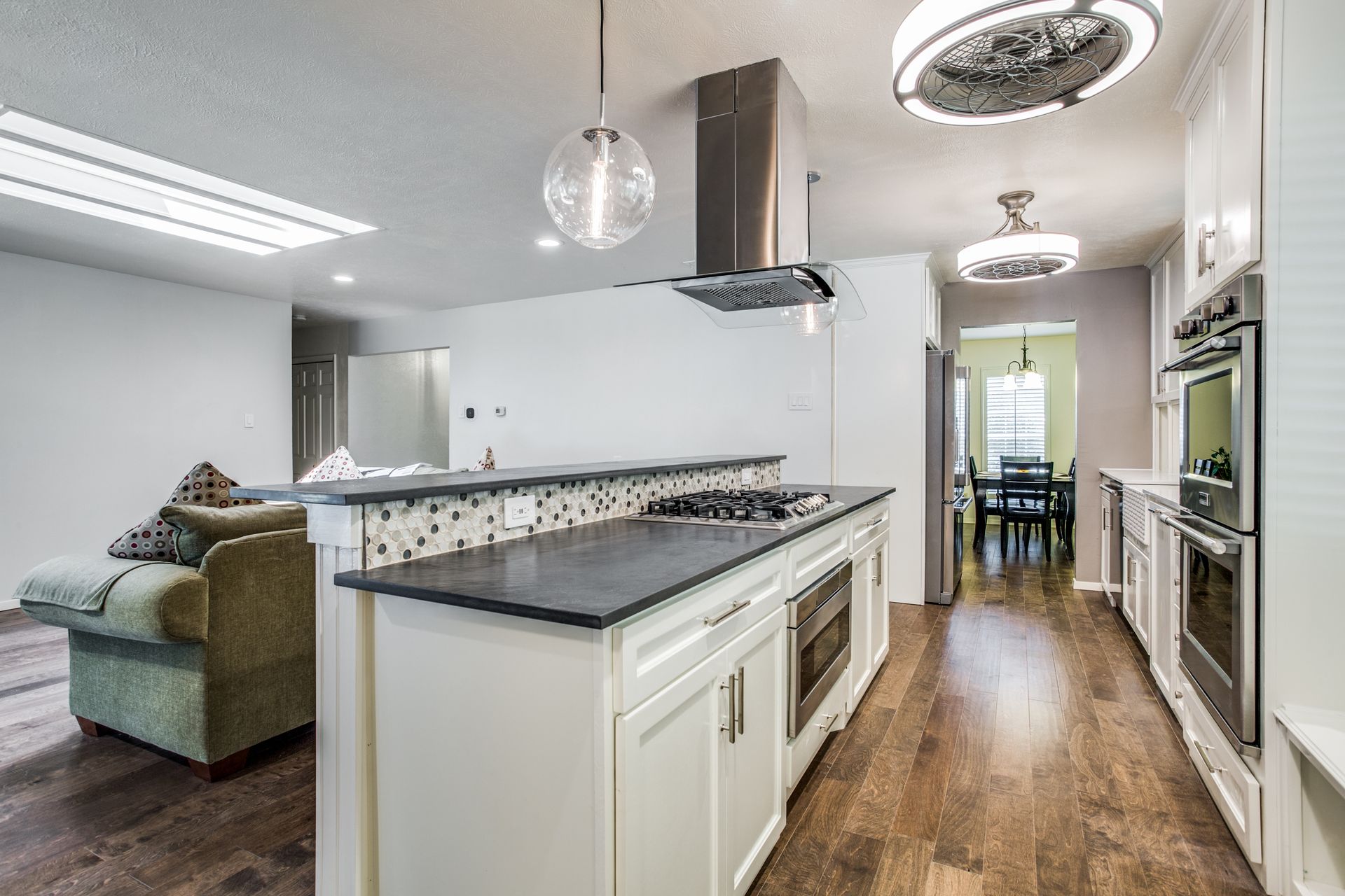 A kitchen with white cabinets , black counter tops , stainless steel appliances and hardwood floors.