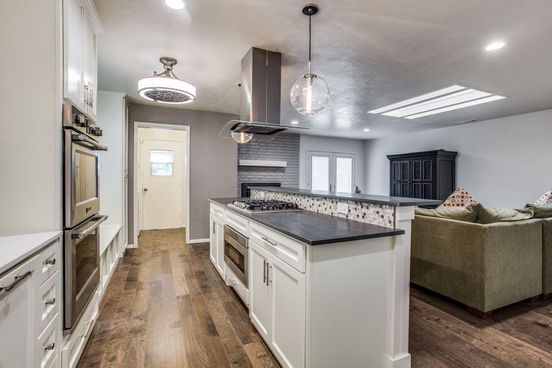 A kitchen with white cabinets , stainless steel appliances , hardwood floors and a large island.