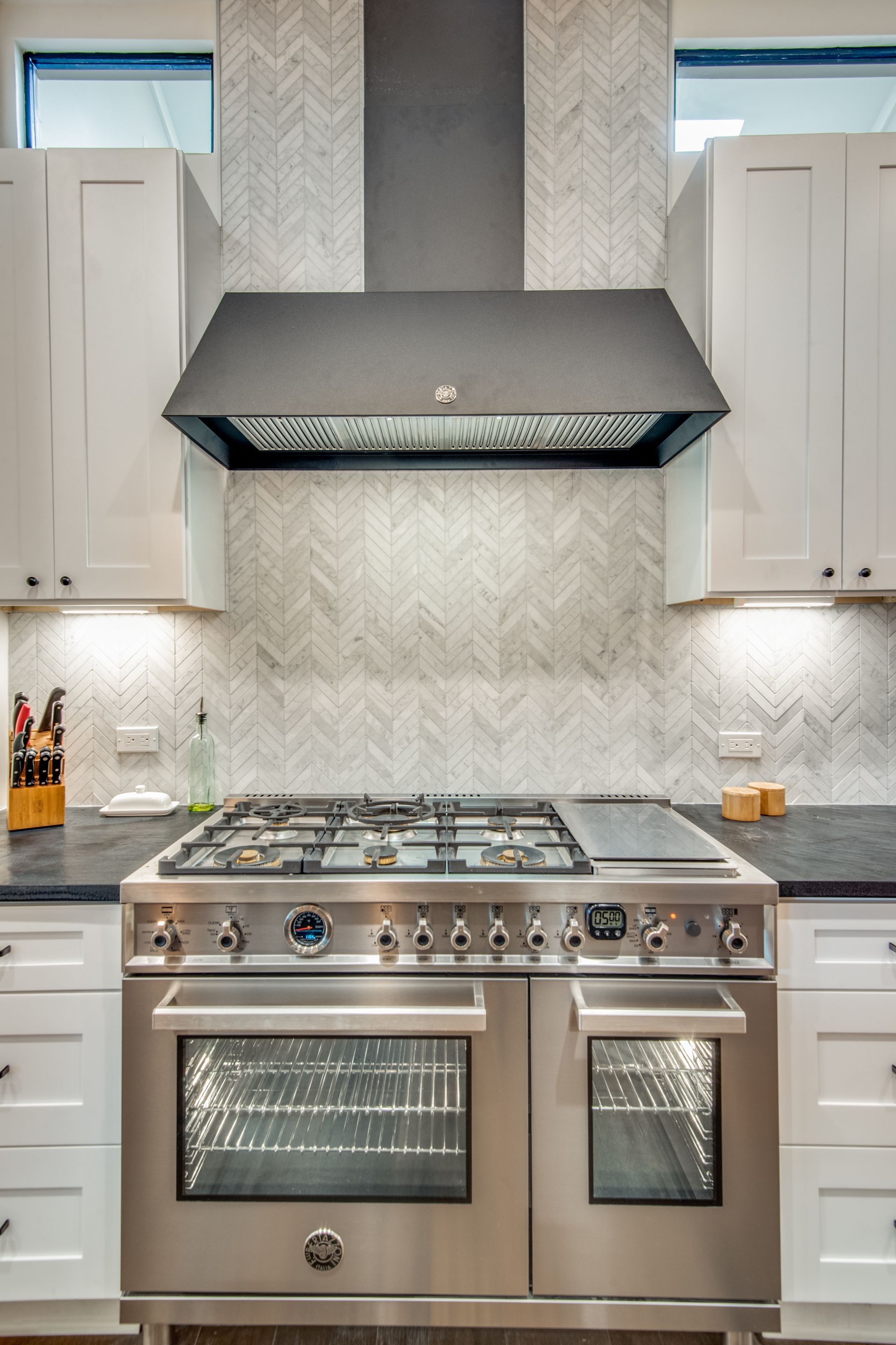 A stainless steel stove with a black hood is in a kitchen.