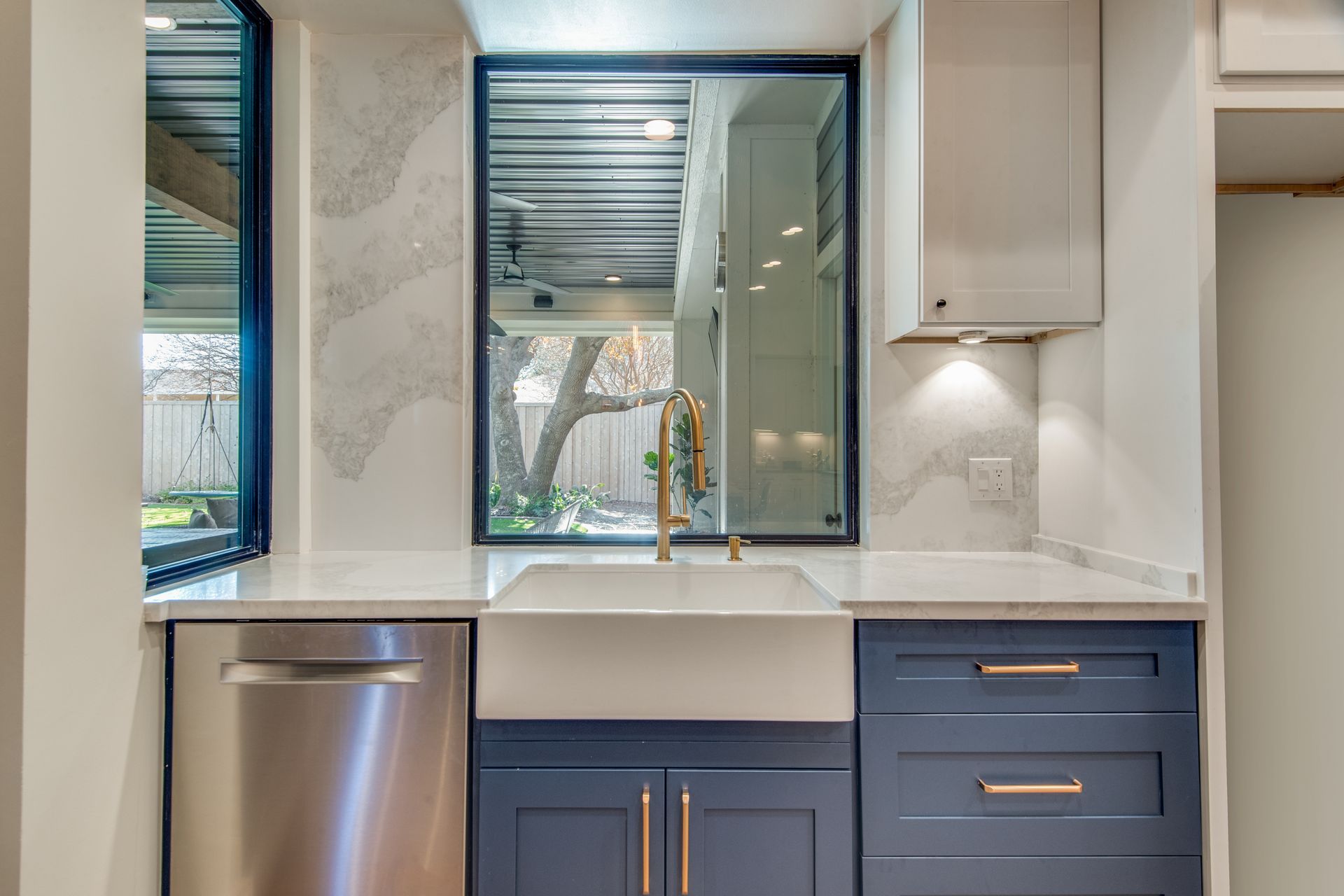 A kitchen with blue cabinets , stainless steel appliances , a sink and a window.
