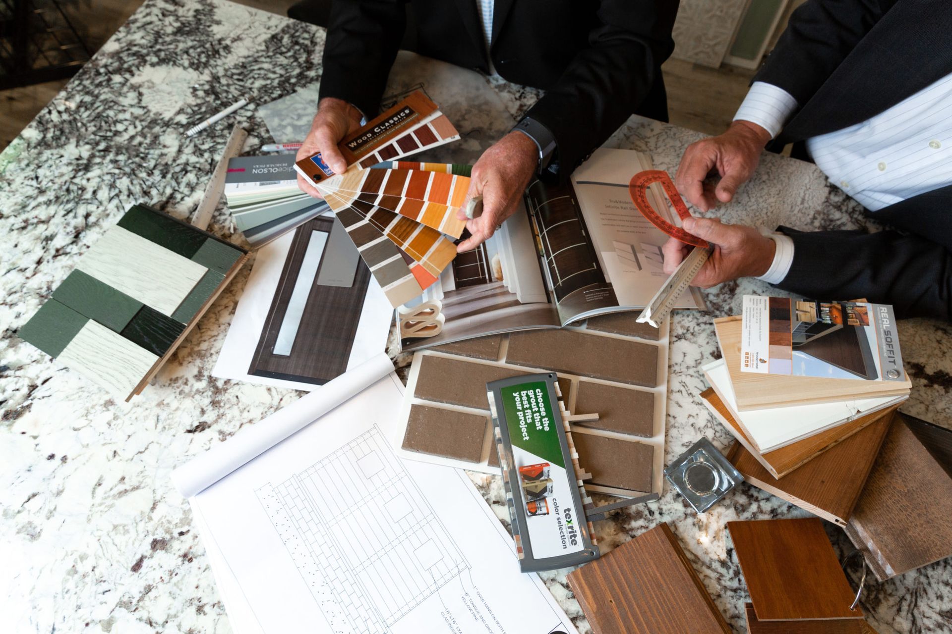 Two men are sitting at a table looking at different types of materials.