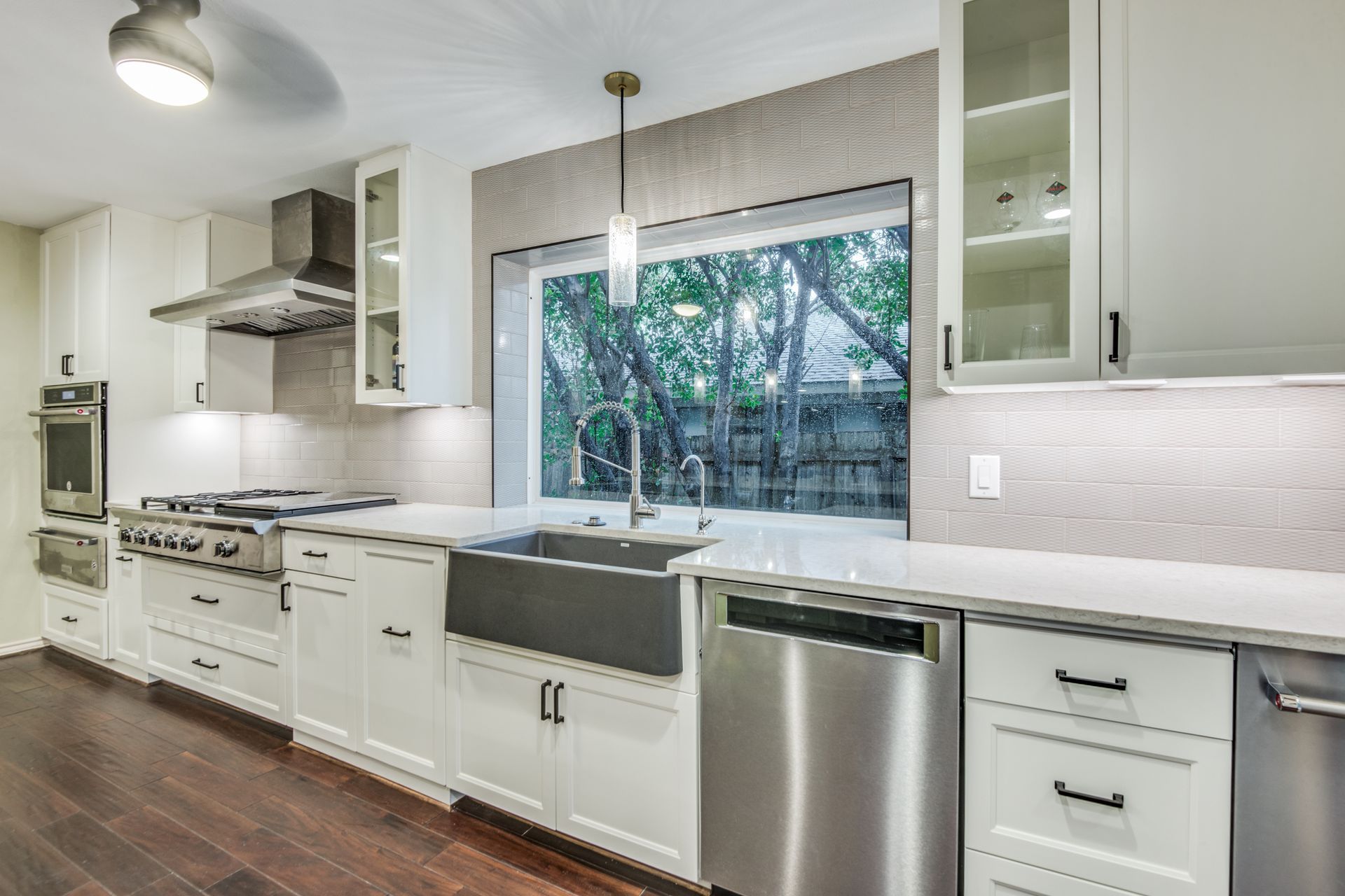 A kitchen with white cabinets , stainless steel appliances , a sink and a window.