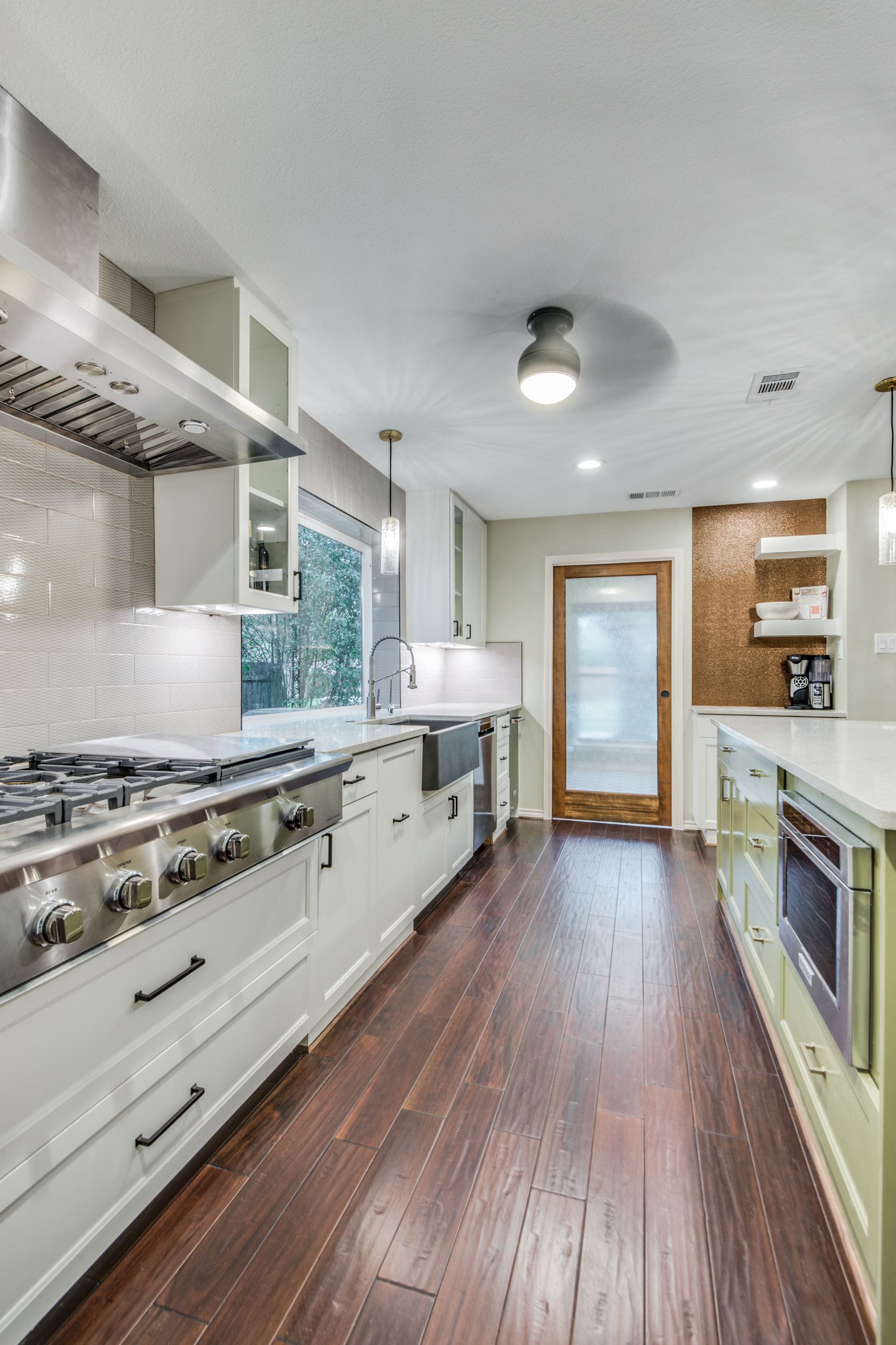 A kitchen with hardwood floors , white cabinets and stainless steel appliances.