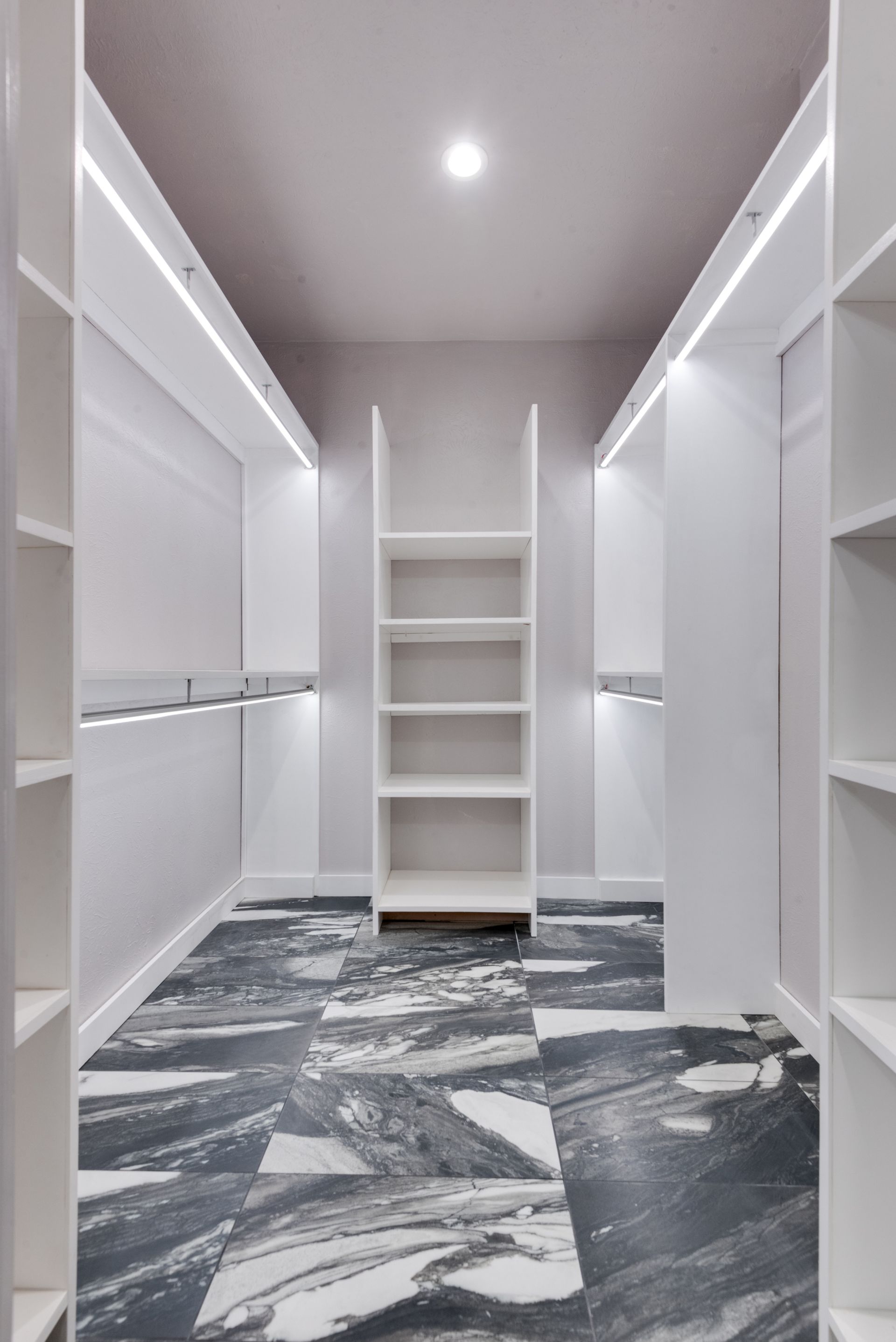 A walk in closet with a marble floor and white shelves.