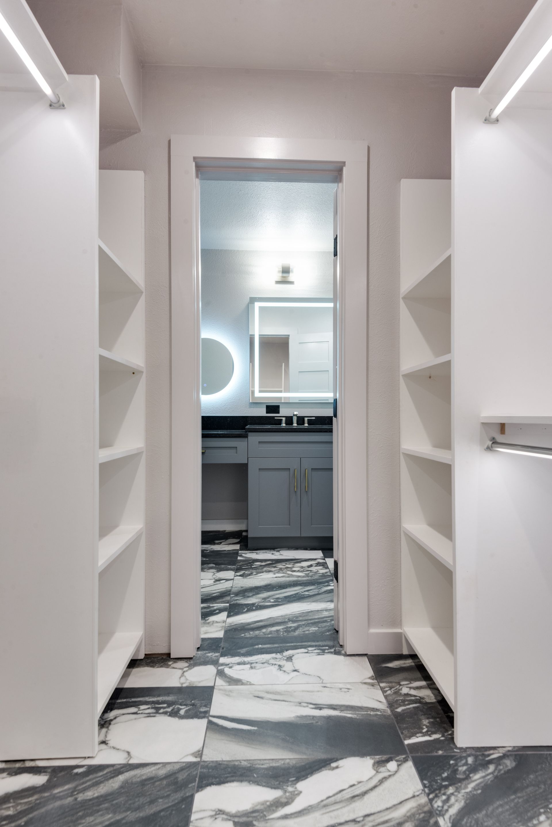 A walk in closet with a bathroom in the background