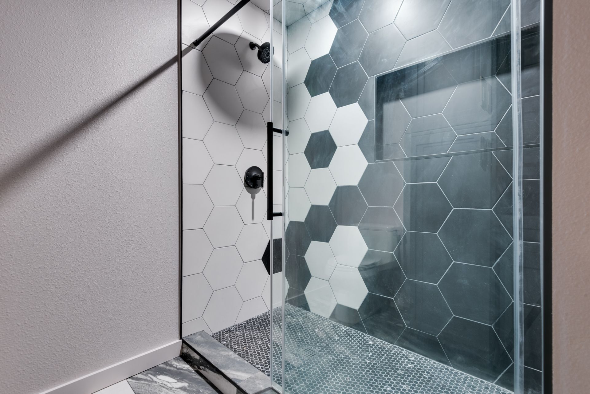 A shower with black and white hexagon tiles and a glass door.