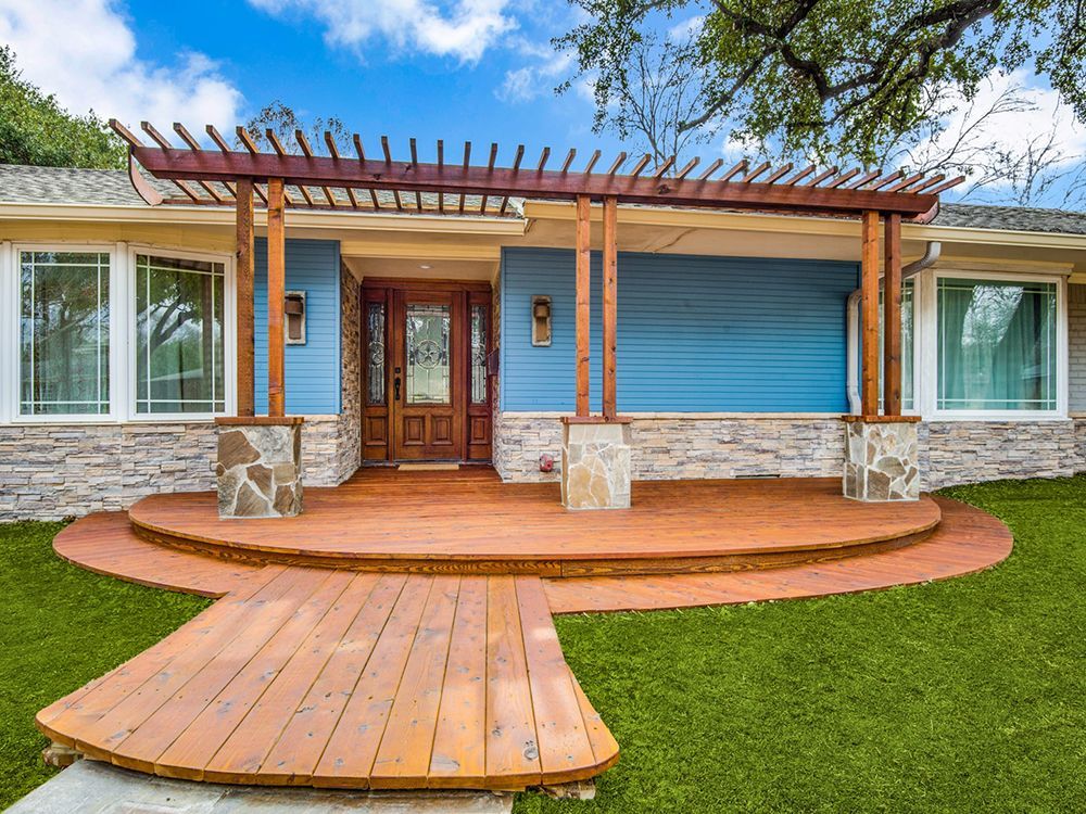 A blue house remodel  with a wooden deck and a pergola over the front porch.