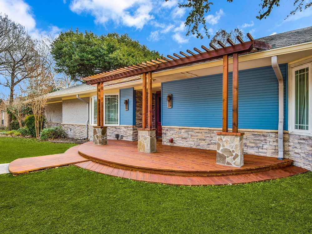 A blue house remodel  with a large porch and a wooden pergola.