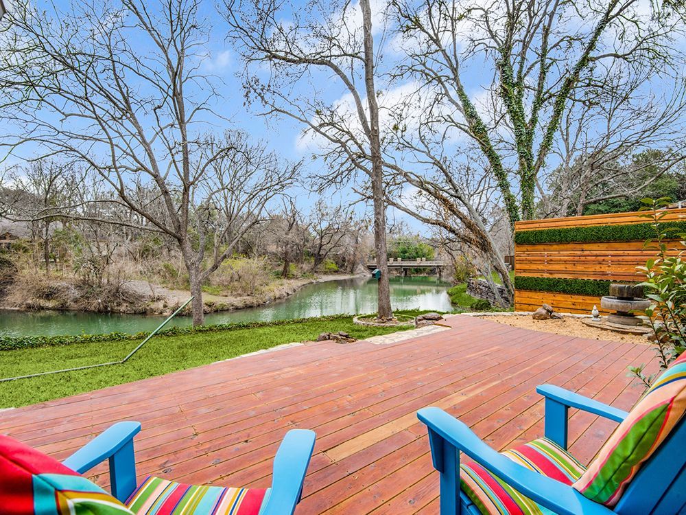 Two blue chairs are sitting on a wooden deck overlooking a river.