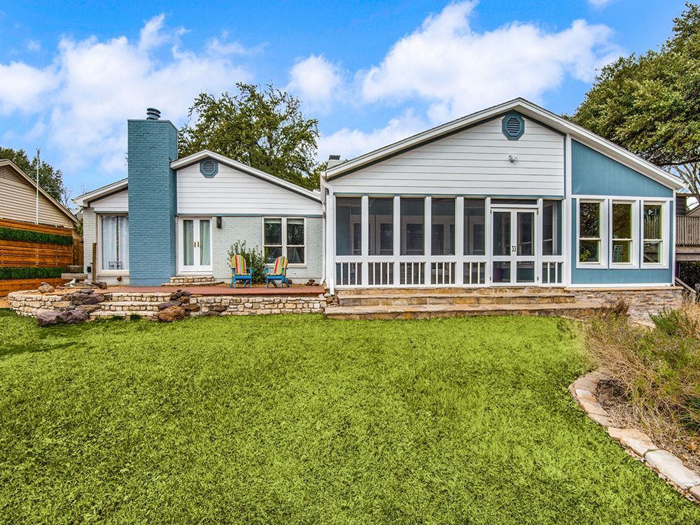 A large house remodel with a screened in porch and a large lawn in front of it.