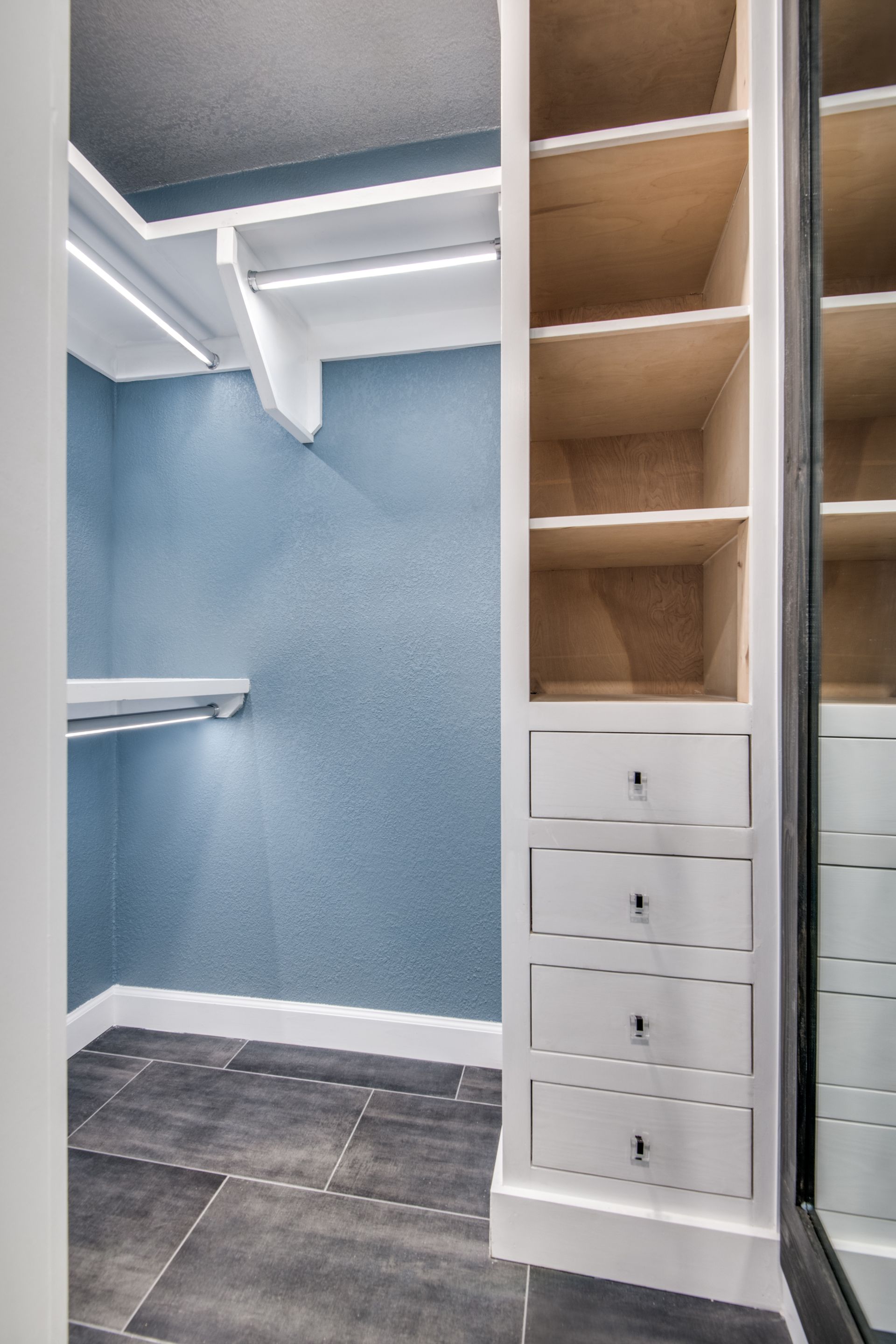A walk in closet remodel with lots of shelves and drawers and a mirror.
